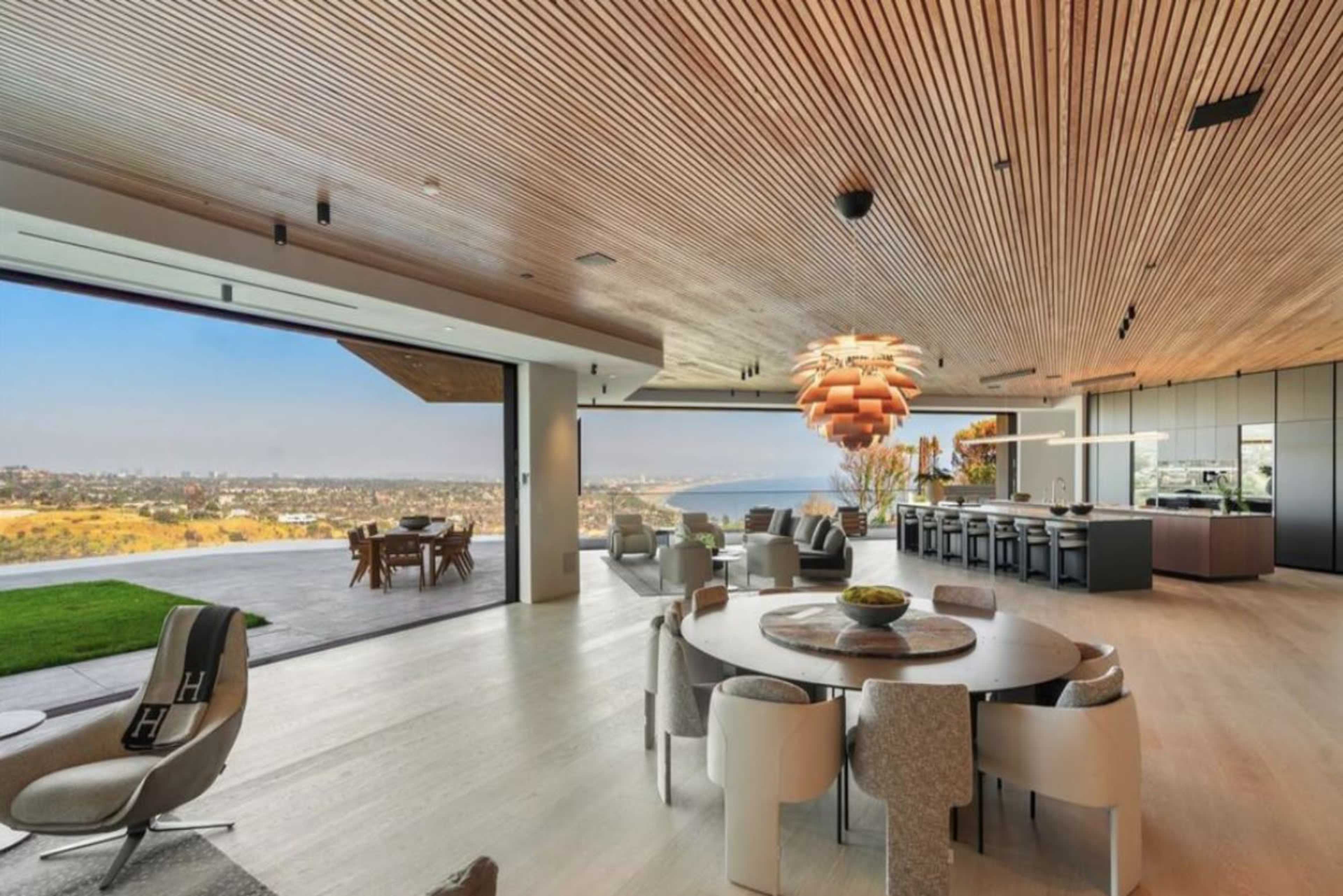 The image depicts a modern, open-concept living space with floor-to-ceiling windows, showcasing a panoramic view of a coastal landscape.
