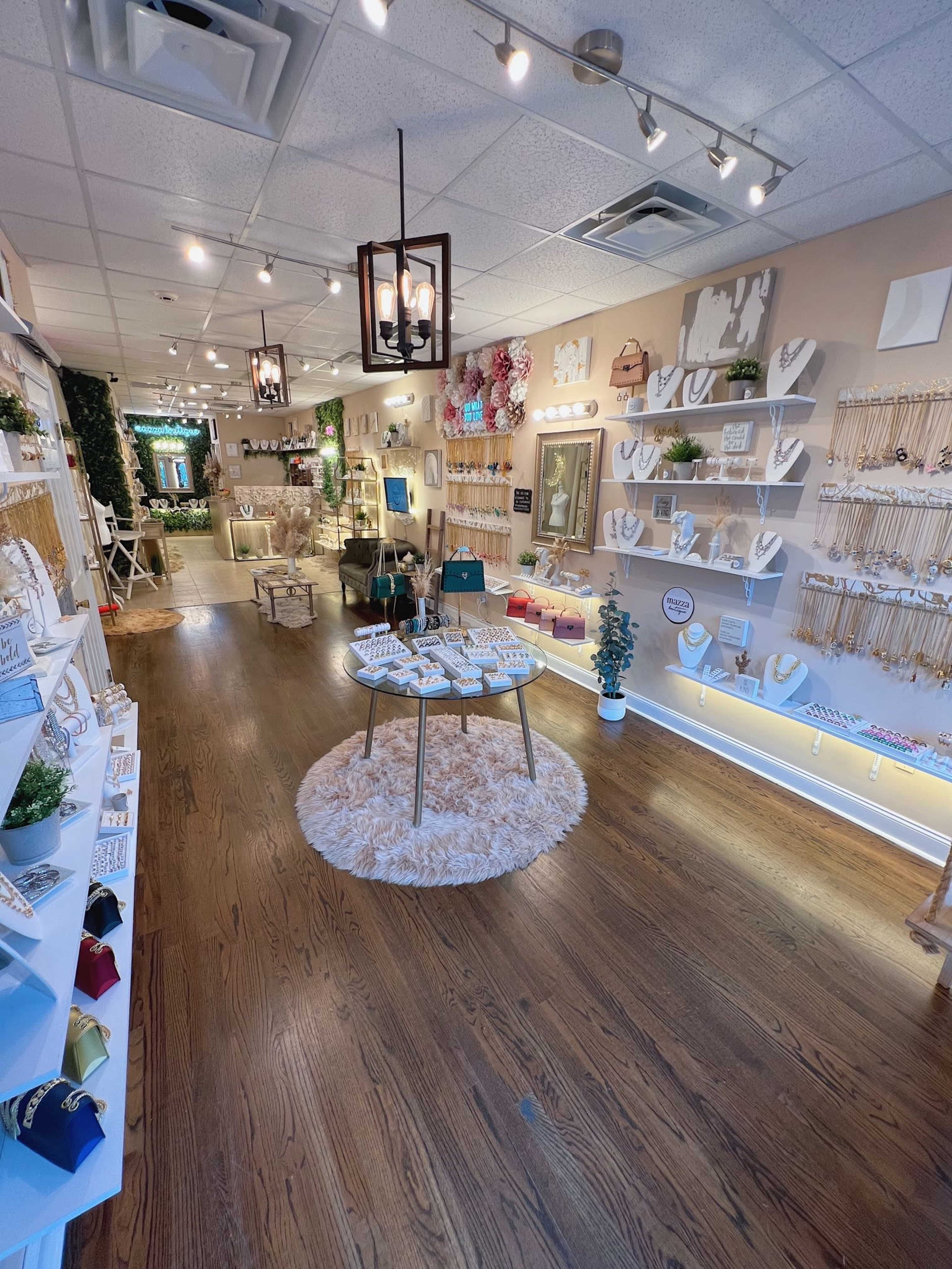 A jewelry store interior features display tables with various jewelry pieces, wall-mounted shelves showcasing more items, and a cozy seating area in the background.