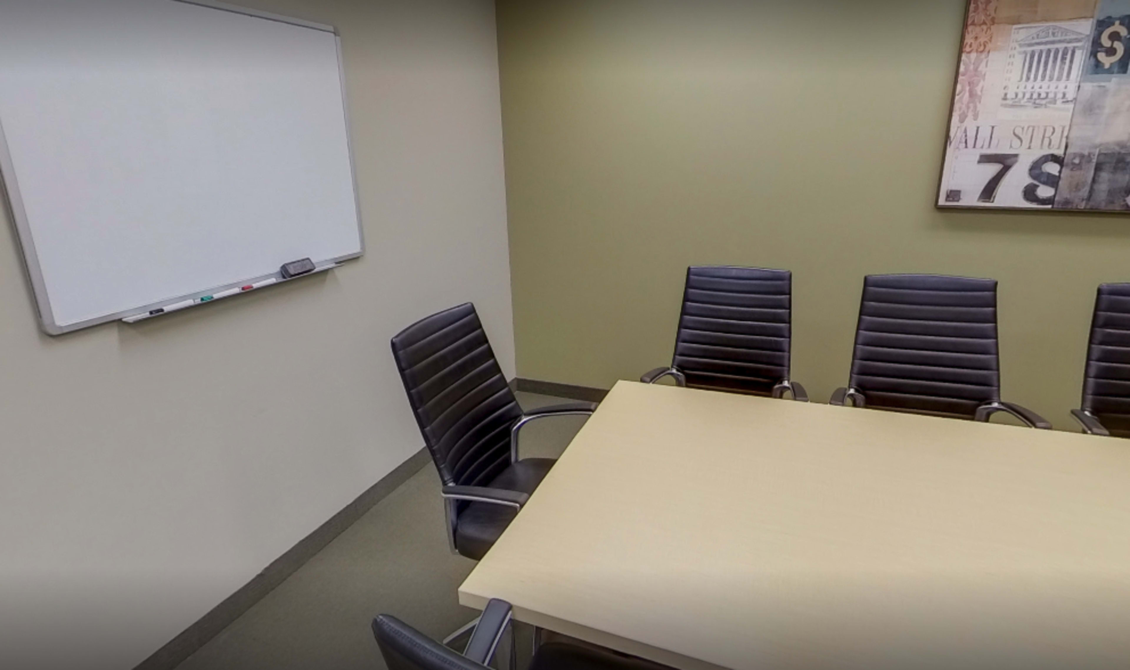 A conference room with a rectangular table surrounded by six black chairs and a whiteboard on the wall.