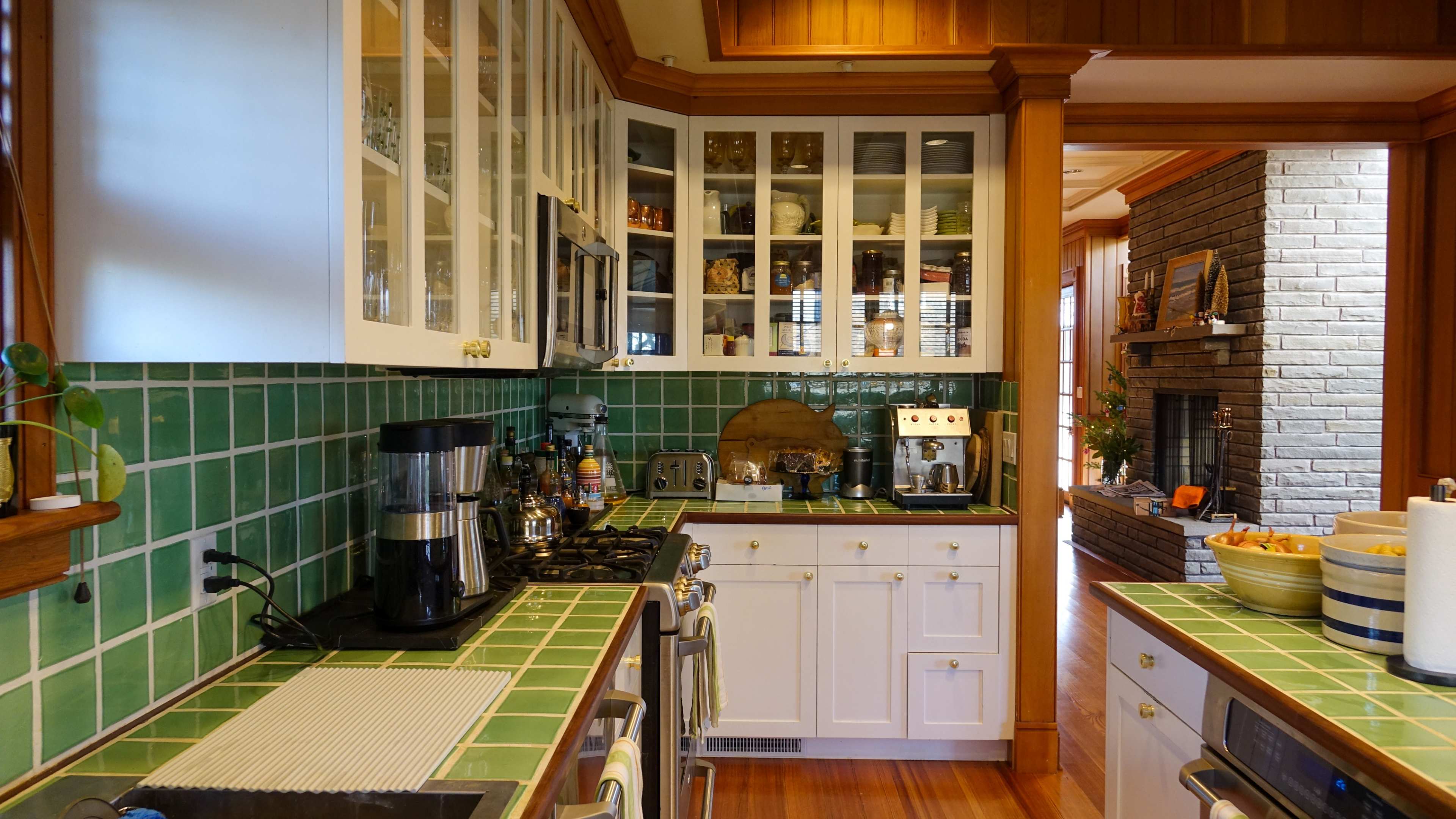 A kitchen featuring green tiled countertops, white cabinets with glass doors, and various kitchen appliances.