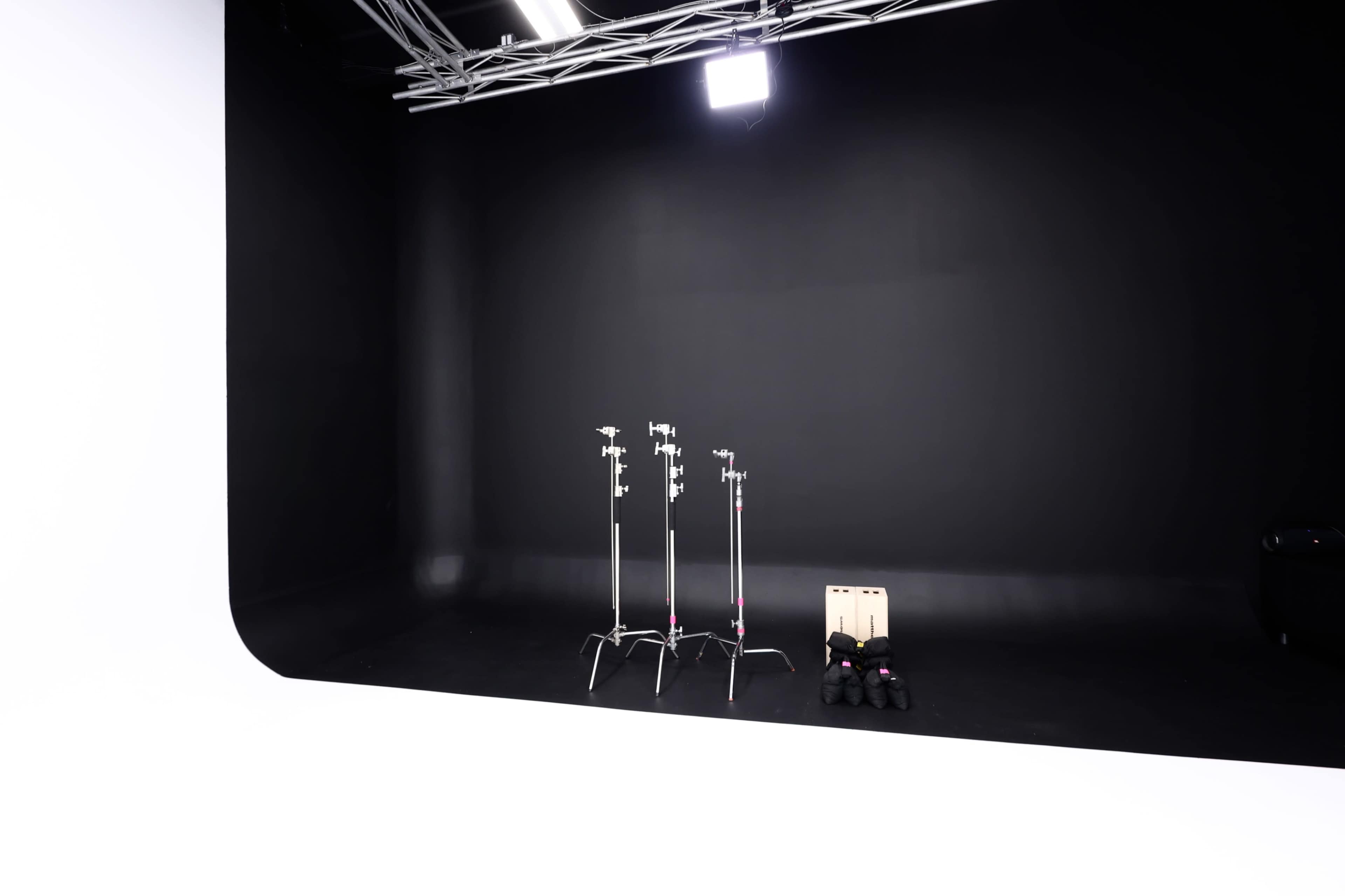 The image shows an empty studio with a black backdrop, two light stands, a wooden box, and a set of black shoes on the floor.