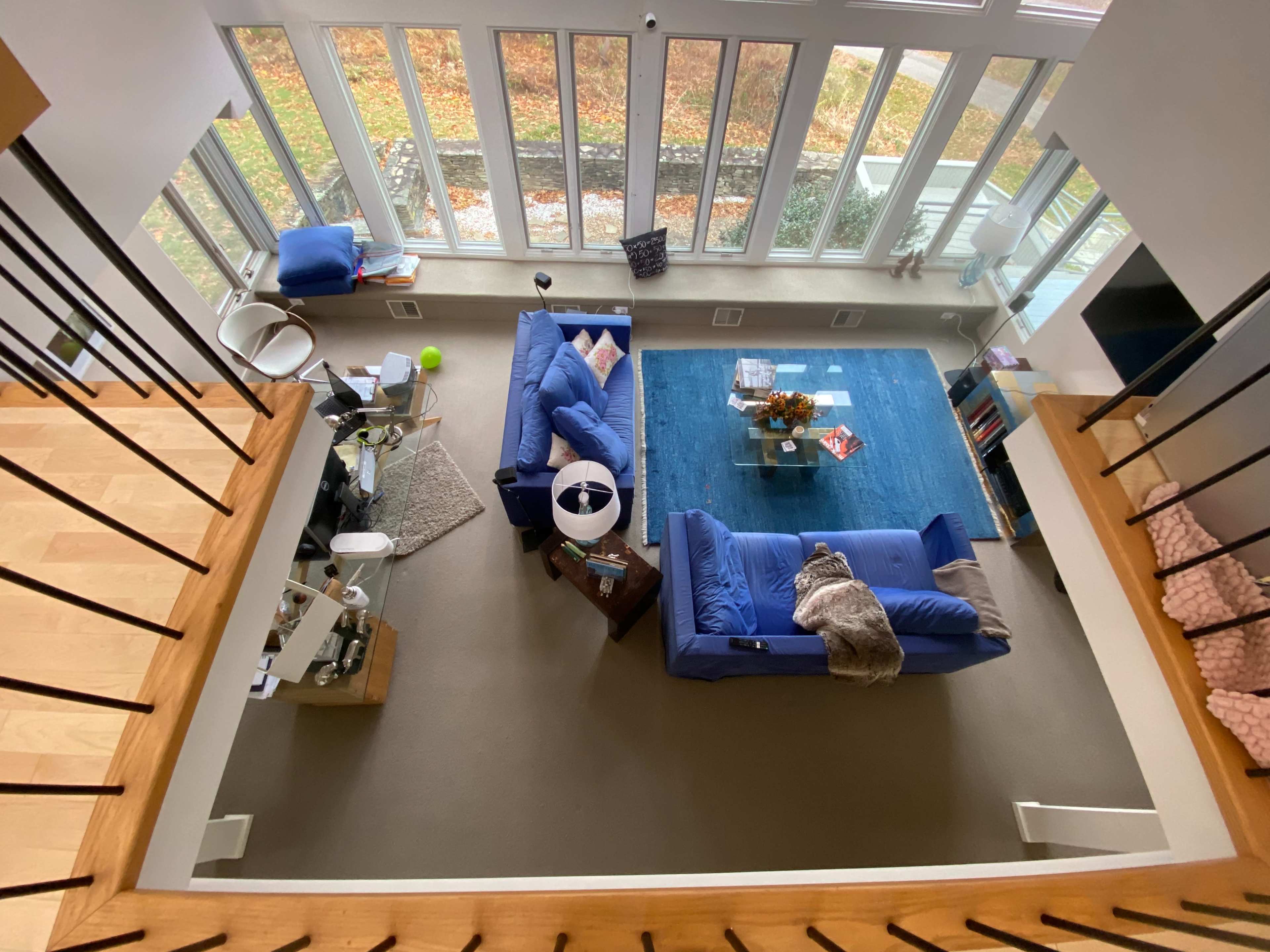 A spacious living room with large windows, two blue sofas, a coffee table, and a blue area rug, viewed from an upper level.
