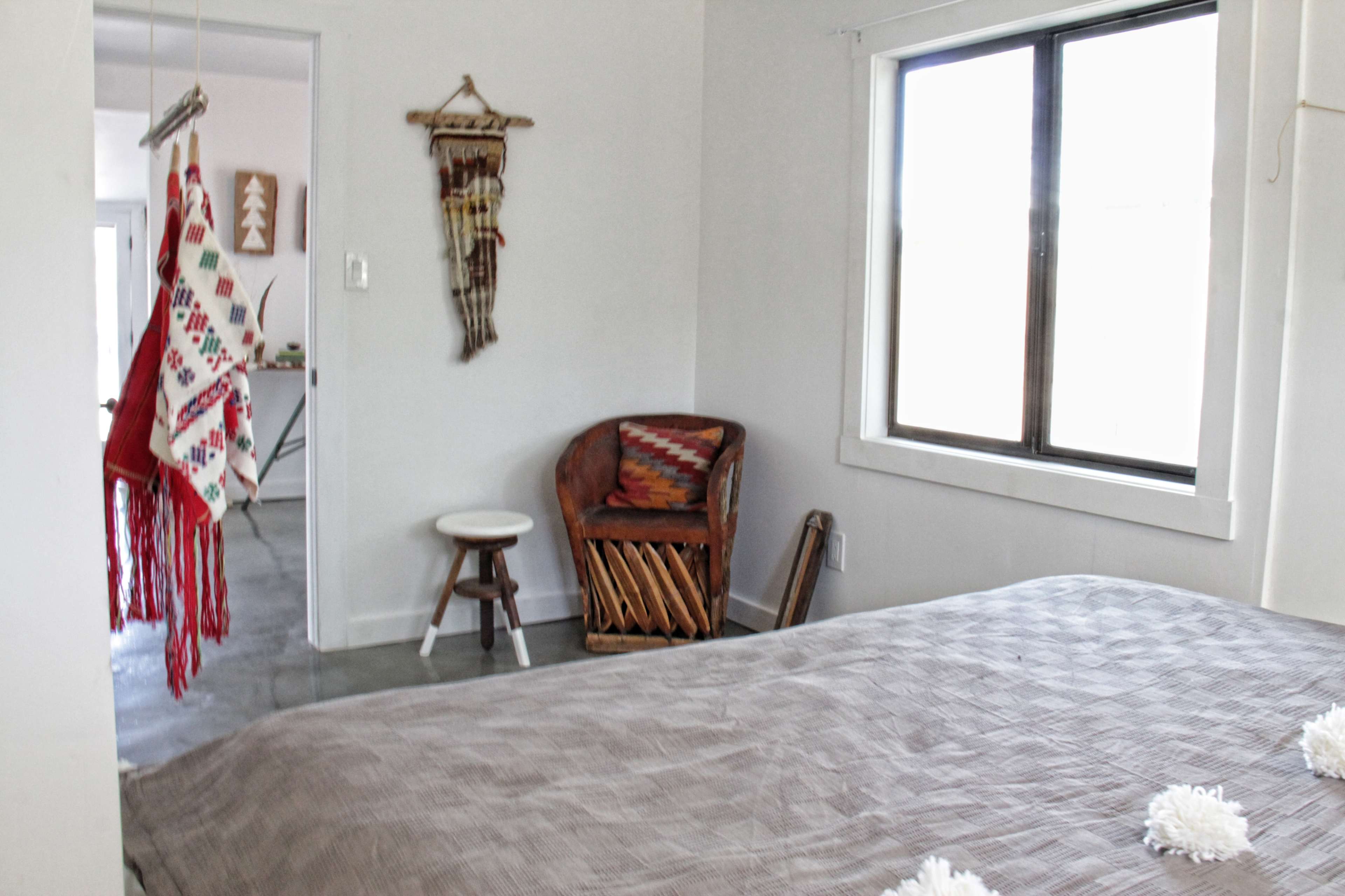 A simple bedroom featuring a bed with a brown cover, a chair in the corner, and hanging decorative items on the wall.