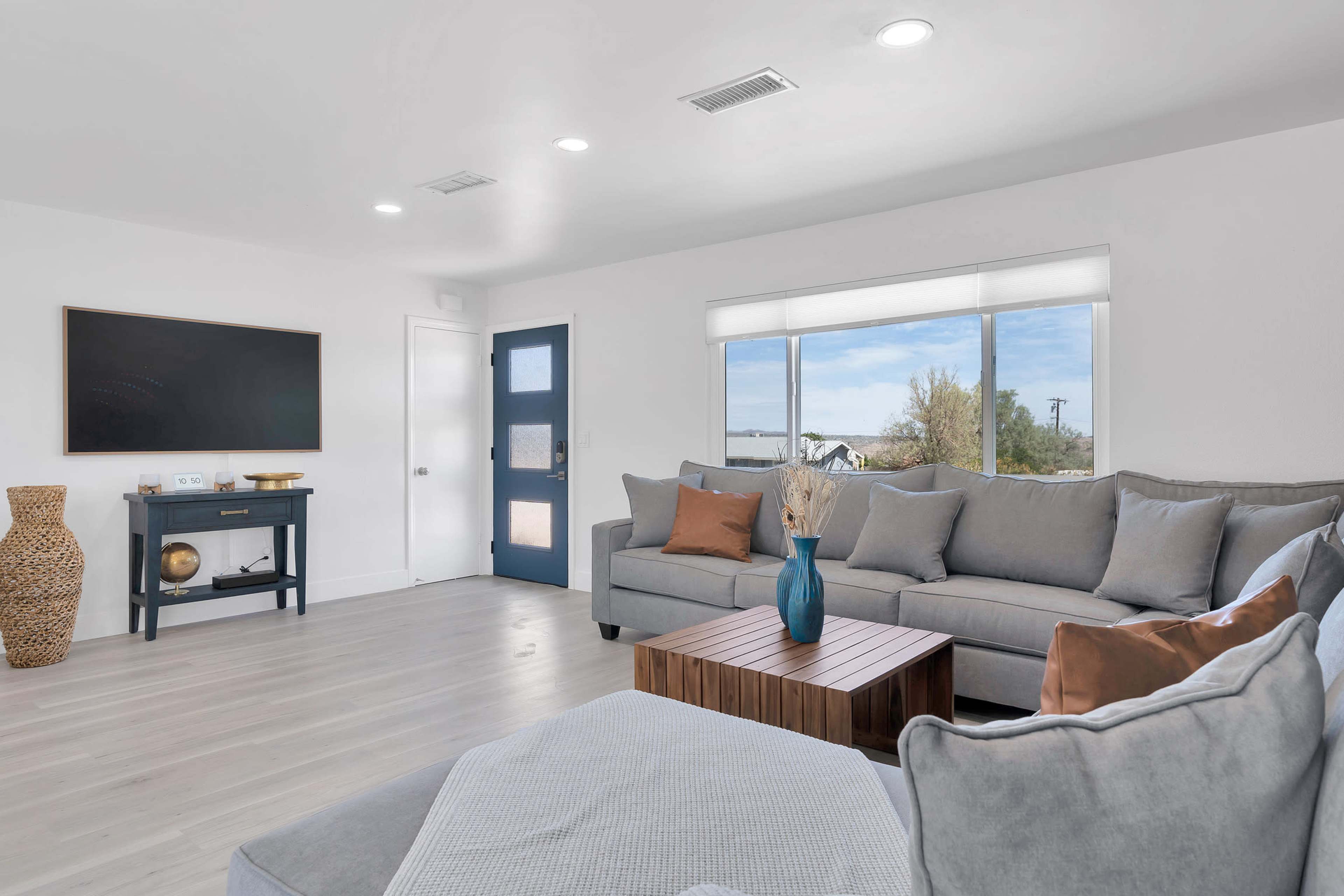 The image shows a modern living room with a gray sectional sofa, a wooden coffee table, and a flat-screen TV mounted on the wall.