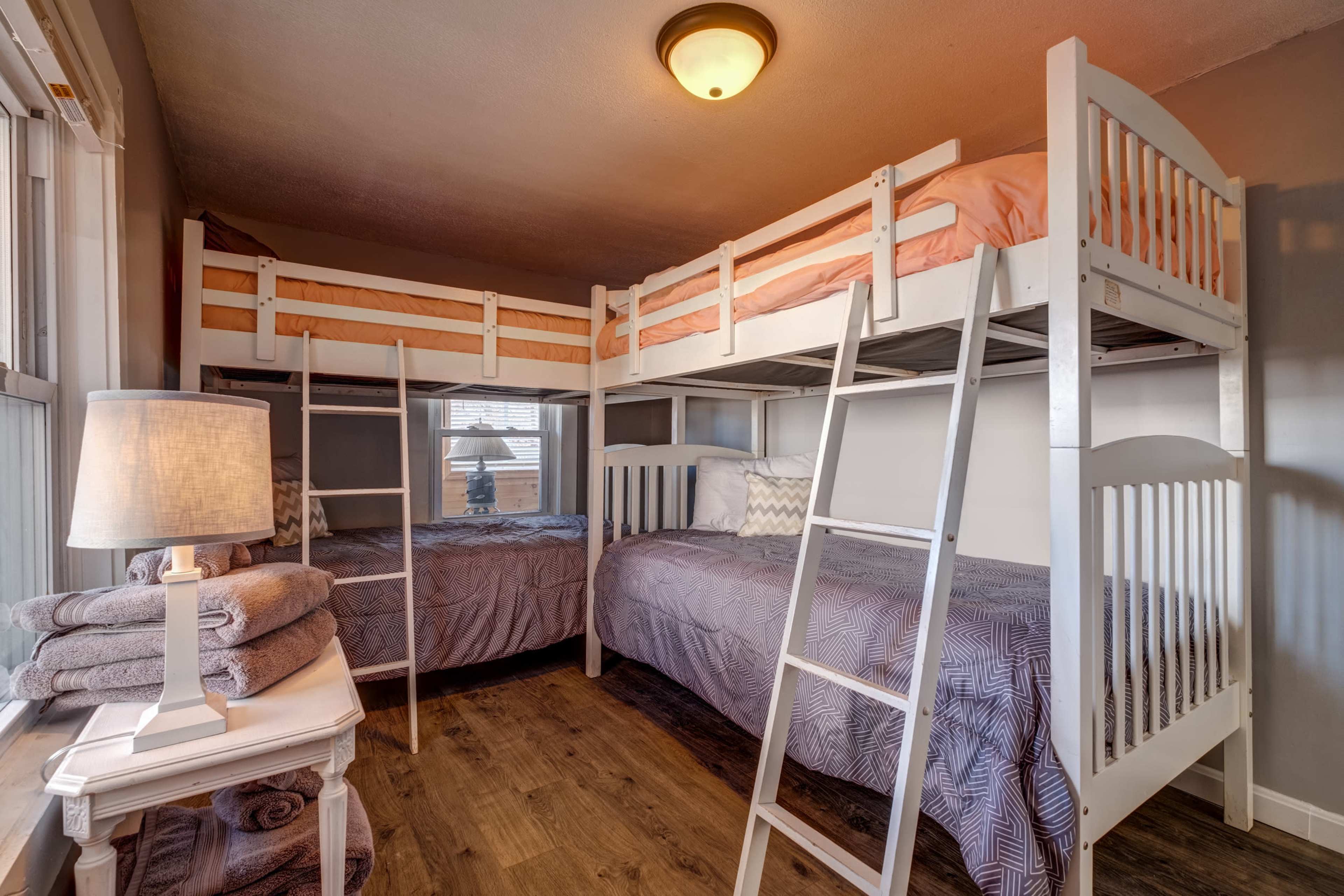 A bedroom with a bunk bed on one side and a twin bed on the other, accompanied by a small bedside table and neatly stacked towels.