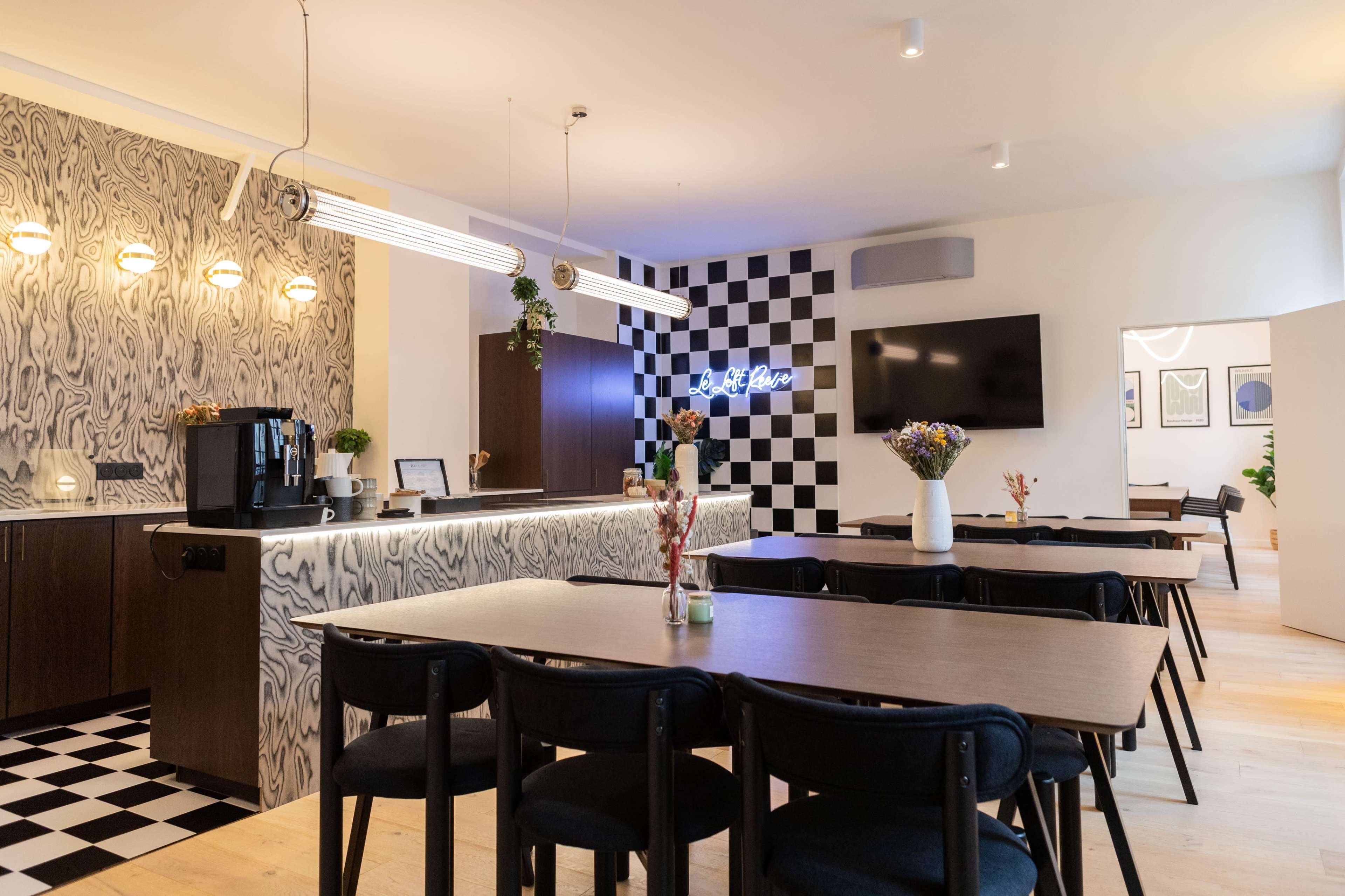 The image shows a modern café interior featuring a checkered black-and-white accent wall, wooden tables, and a coffee station with stylish lighting.
