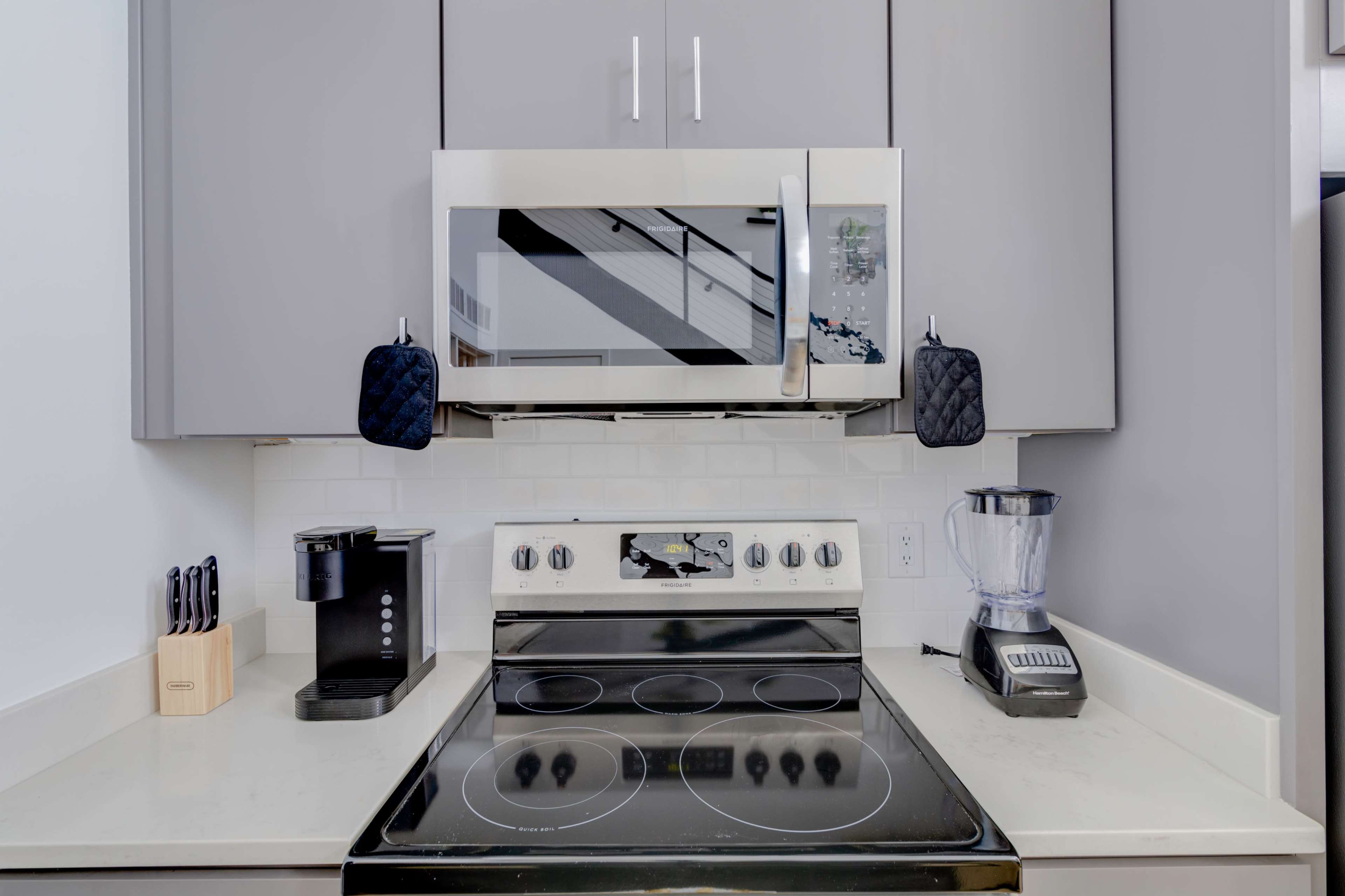 A modern kitchen with a stove, microwave, coffee maker, and blender neatly arranged on a countertop.