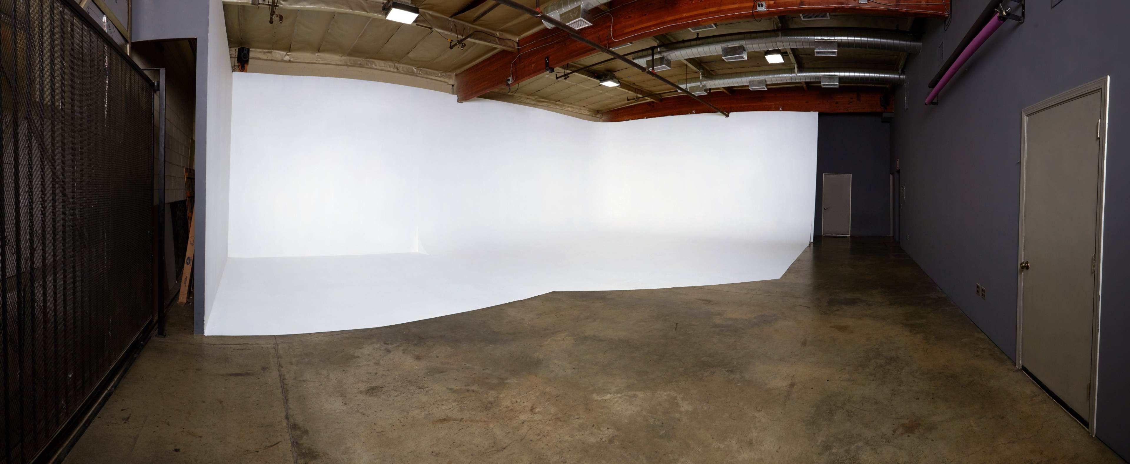 A spacious photo studio with a seamless white backdrop and a concrete floor.