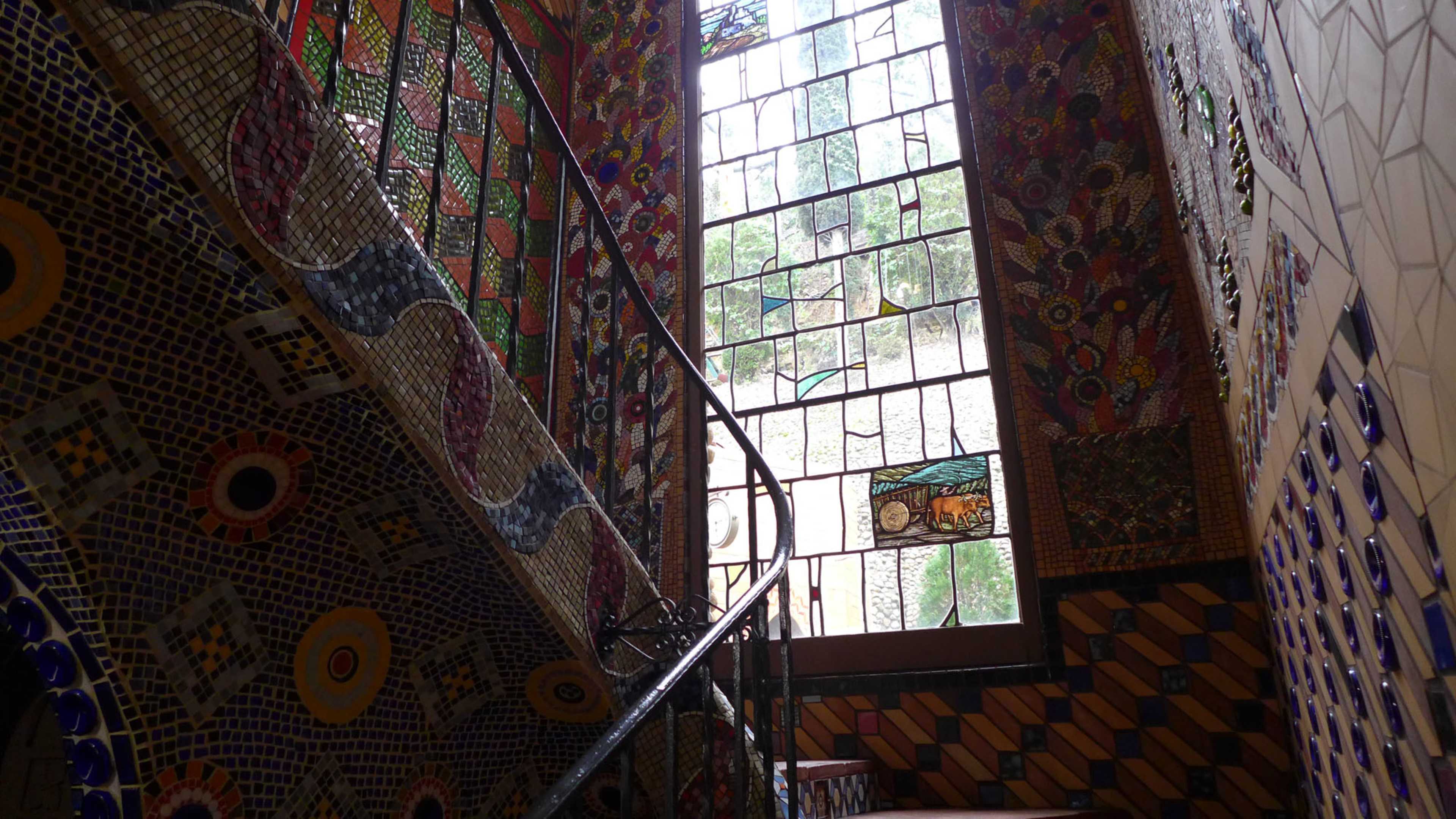 The image shows a colorful, tiled staircase leading to a large stained glass window adorned with intricate designs.