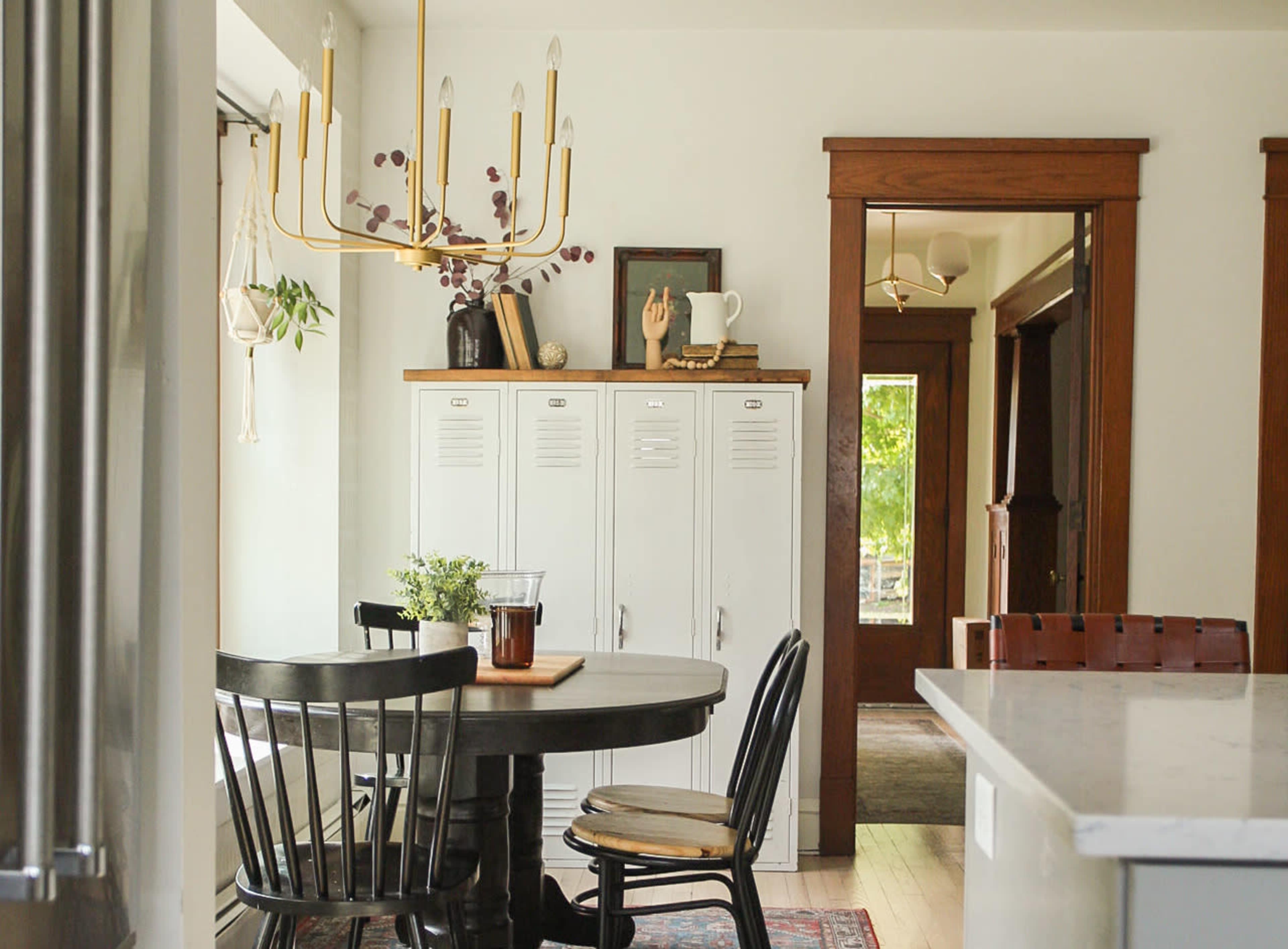 A kitchen features a round black table with chairs, a white locker-style storage unit, and a chandelier overhead.