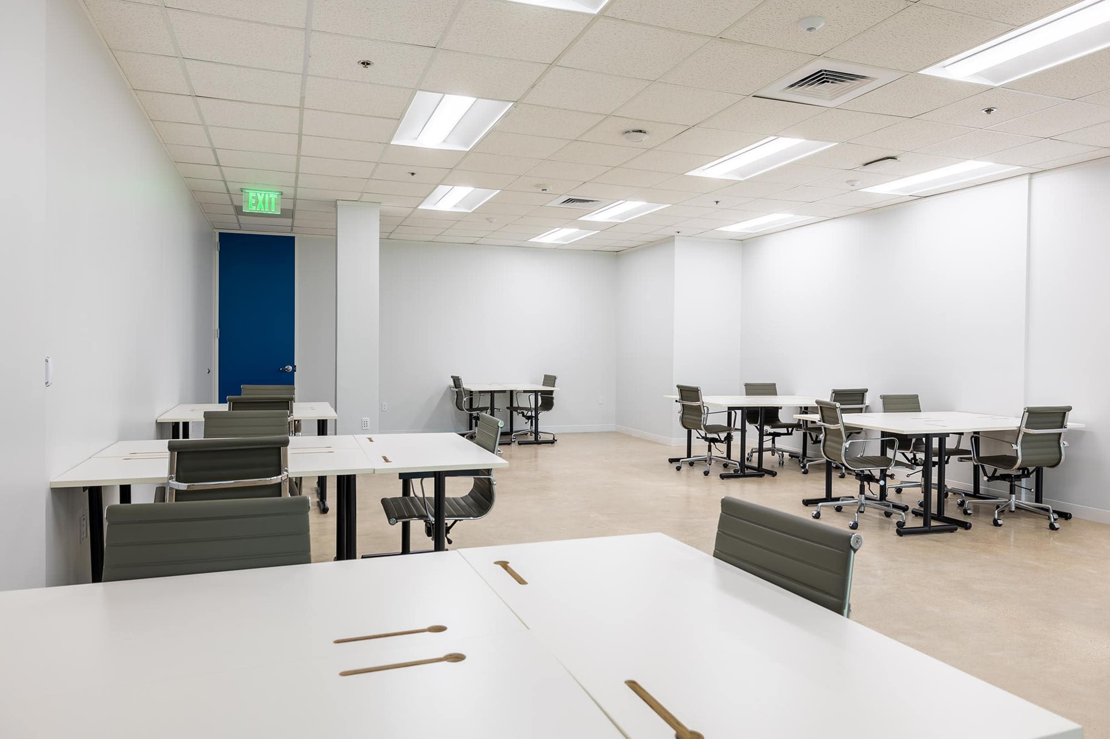 The image shows a large, empty office space with several desks and chairs arranged throughout the room.