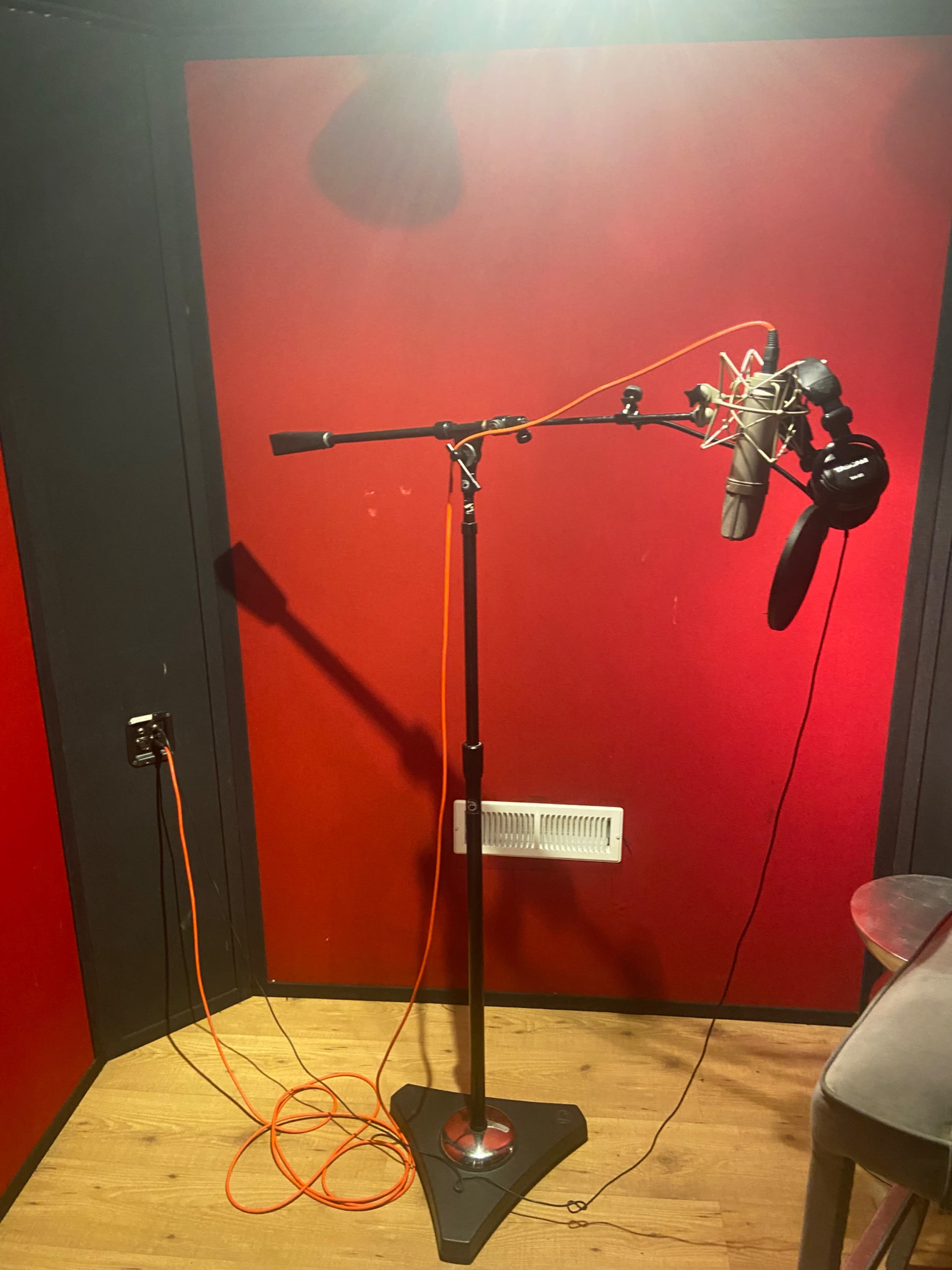 The image shows a microphone stand with a microphone and headphones set up in a room with red walls and a wooden floor.