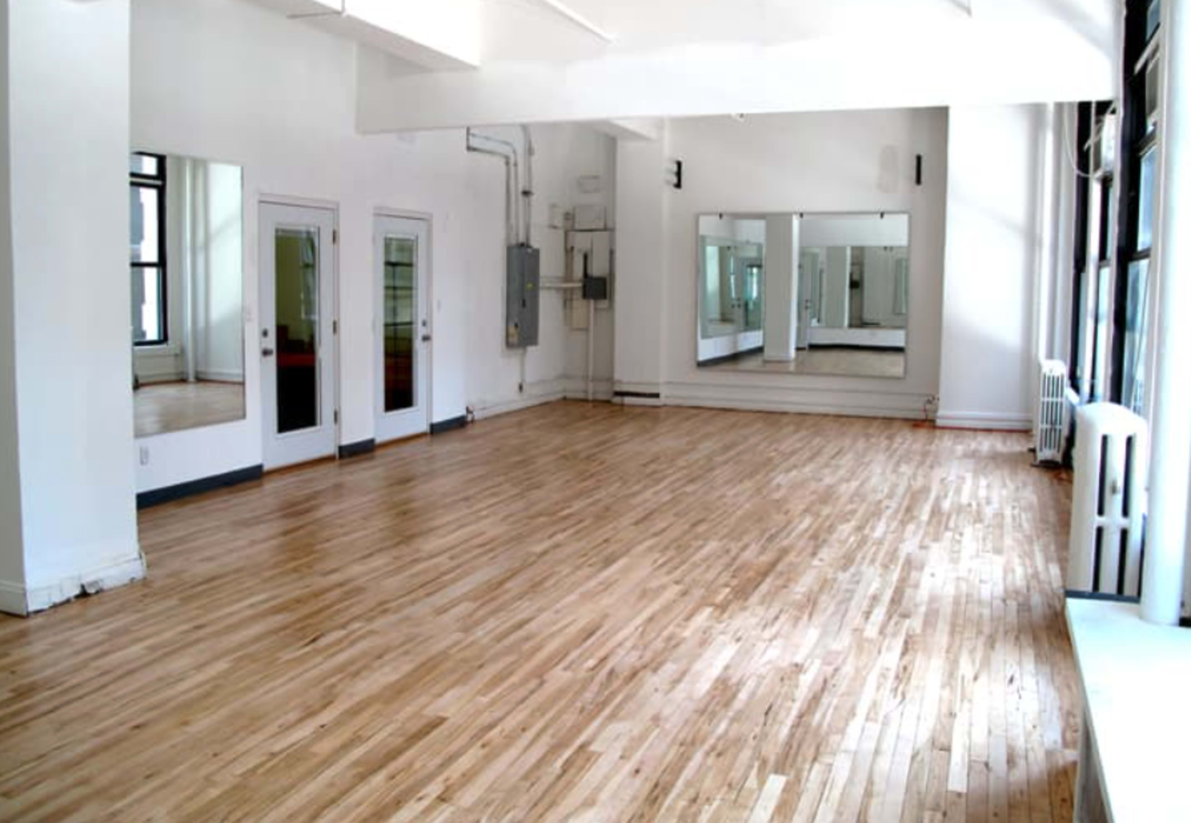 A bright, spacious room with polished wooden floors and large mirrors on one wall.
