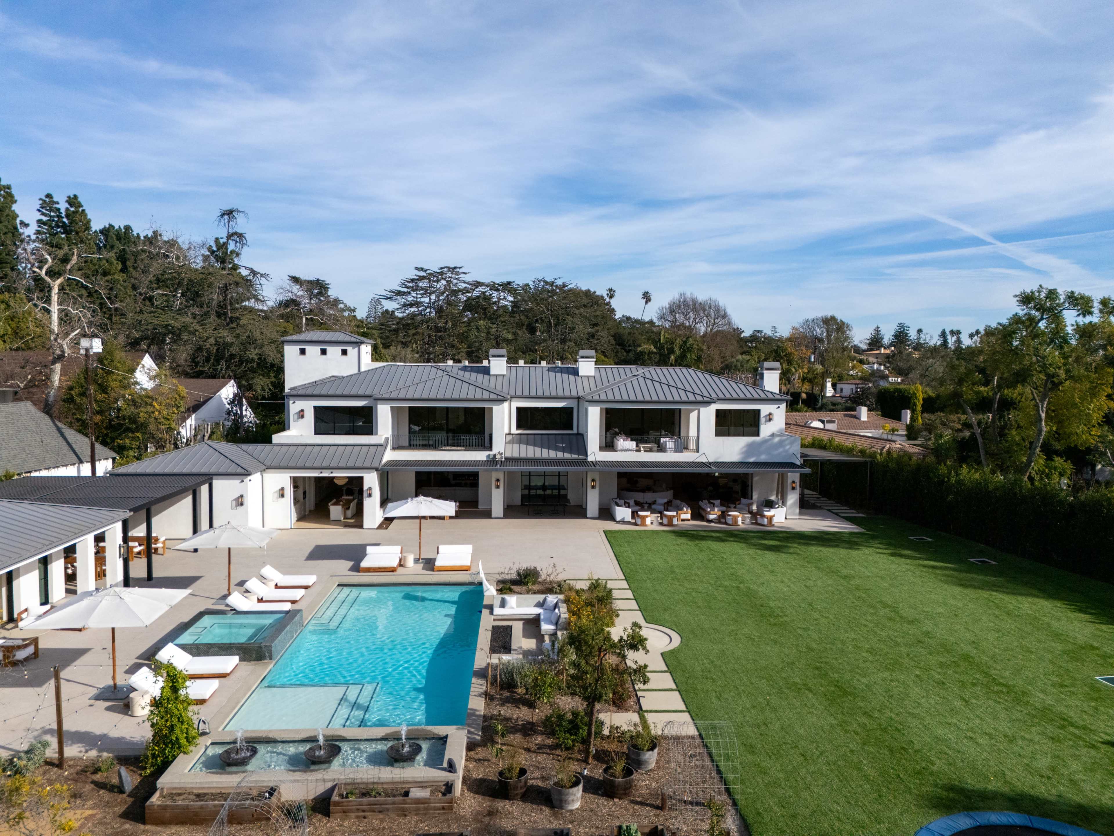 The image shows a modern house with a swimming pool and outdoor seating area, situated on a spacious lawn with trees in the background.