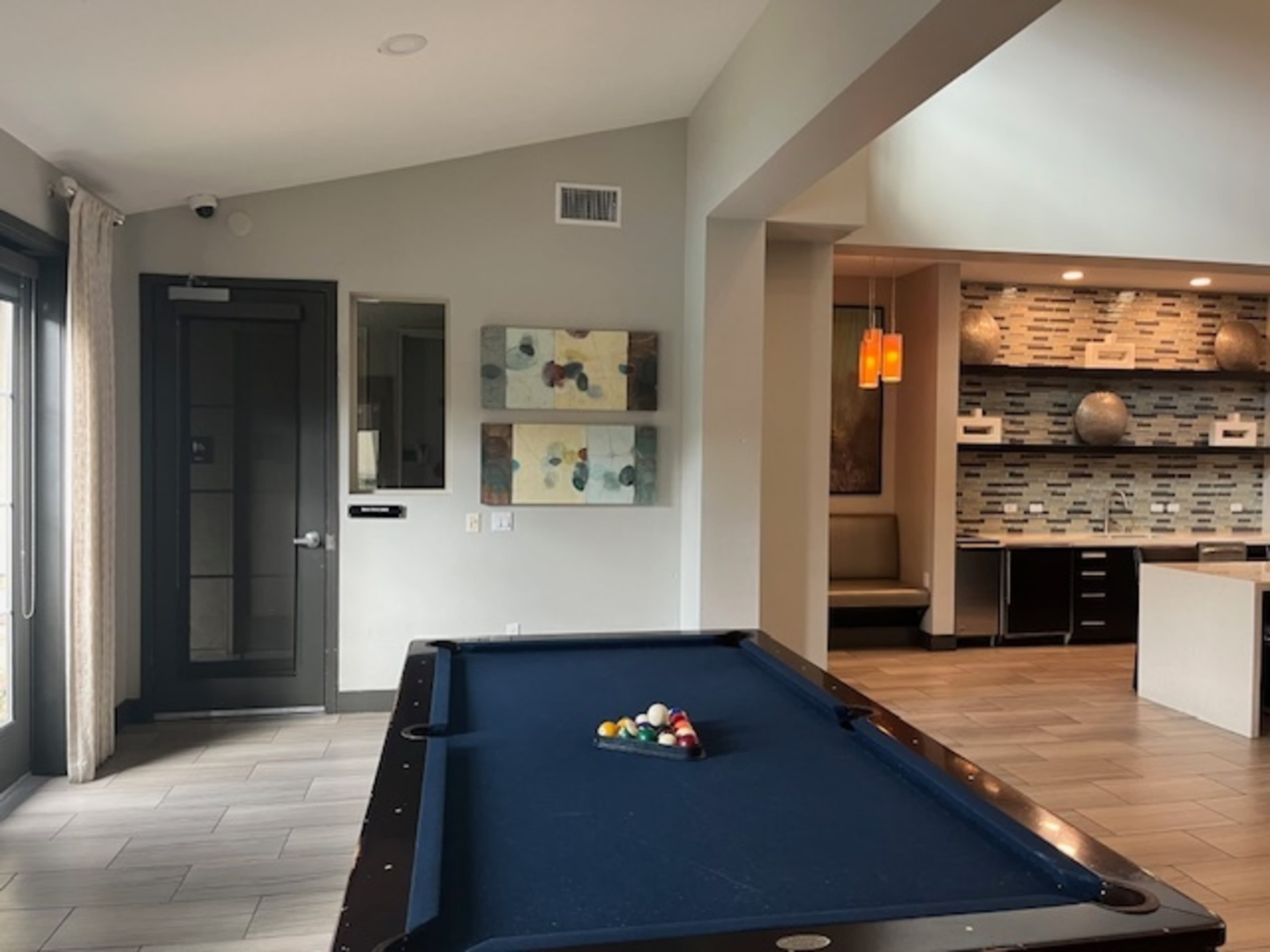 A billiard table with balls racked up is positioned in a modern lounge area featuring a large open space and decorative wall art.