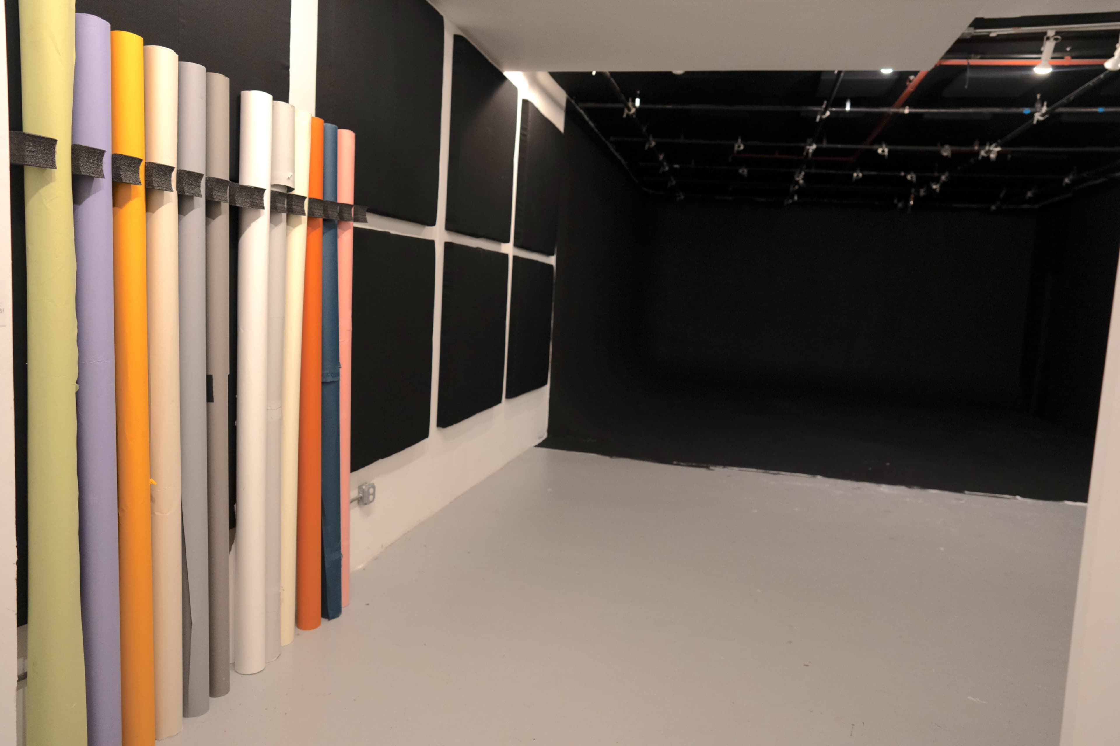 The image shows a photography studio with a collection of colored backdrop rolls on the left and a dark, uncluttered area for shooting on the right.