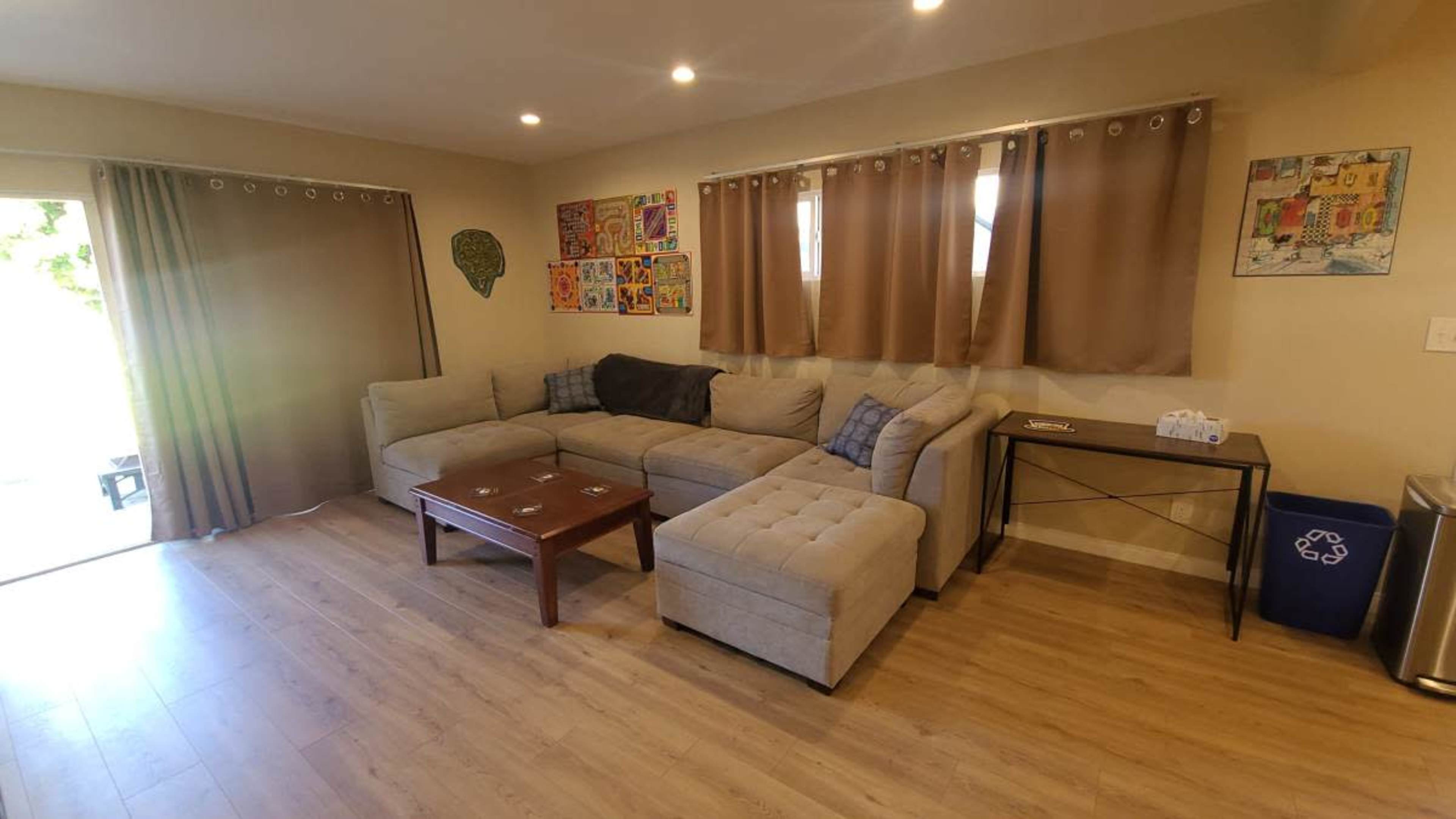 The image shows a living room with a sectional sofa, a wooden coffee table, and curtains, along with a door leading outside.