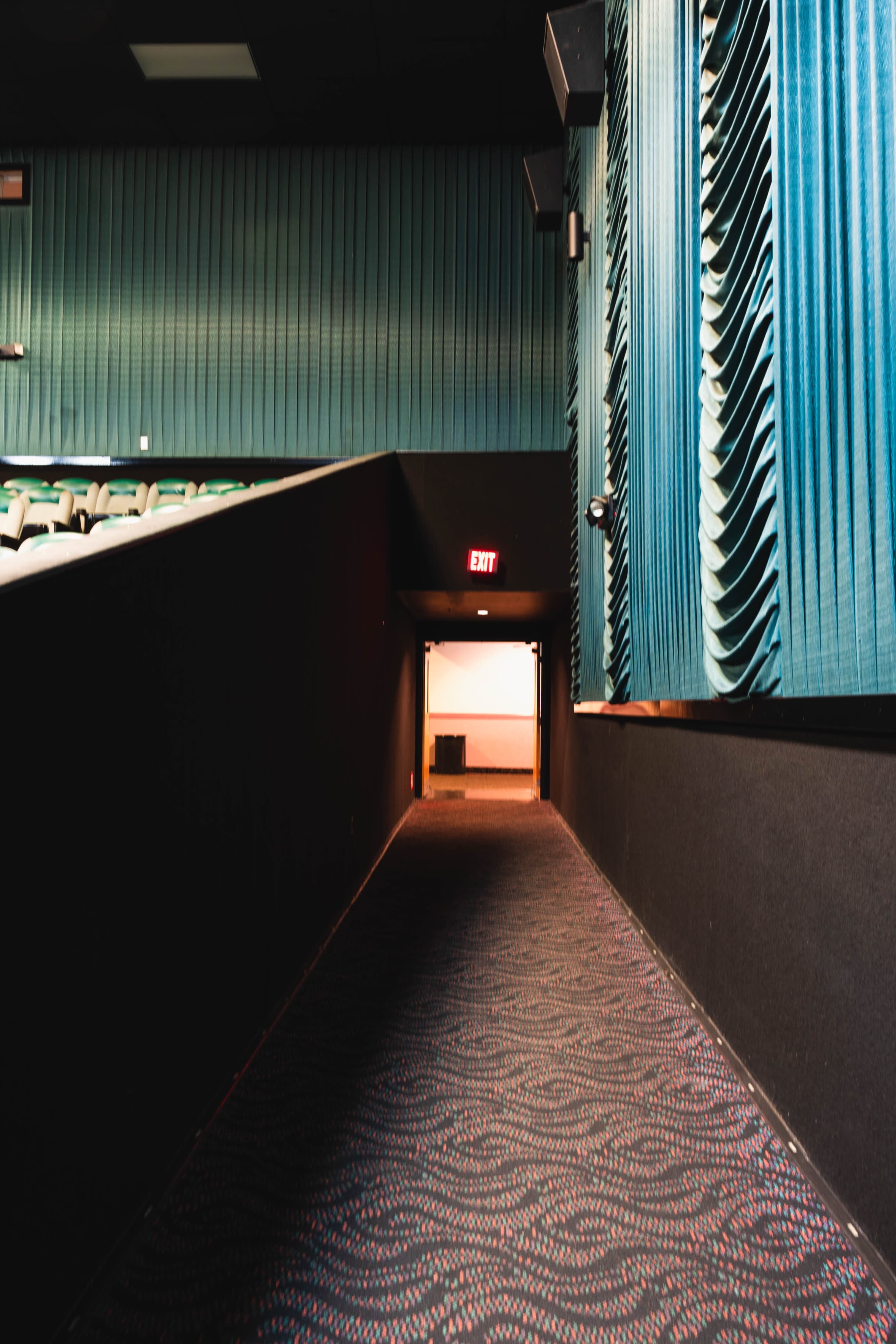 A dimly lit corridor in a theater, leading to an exit door at the far end.