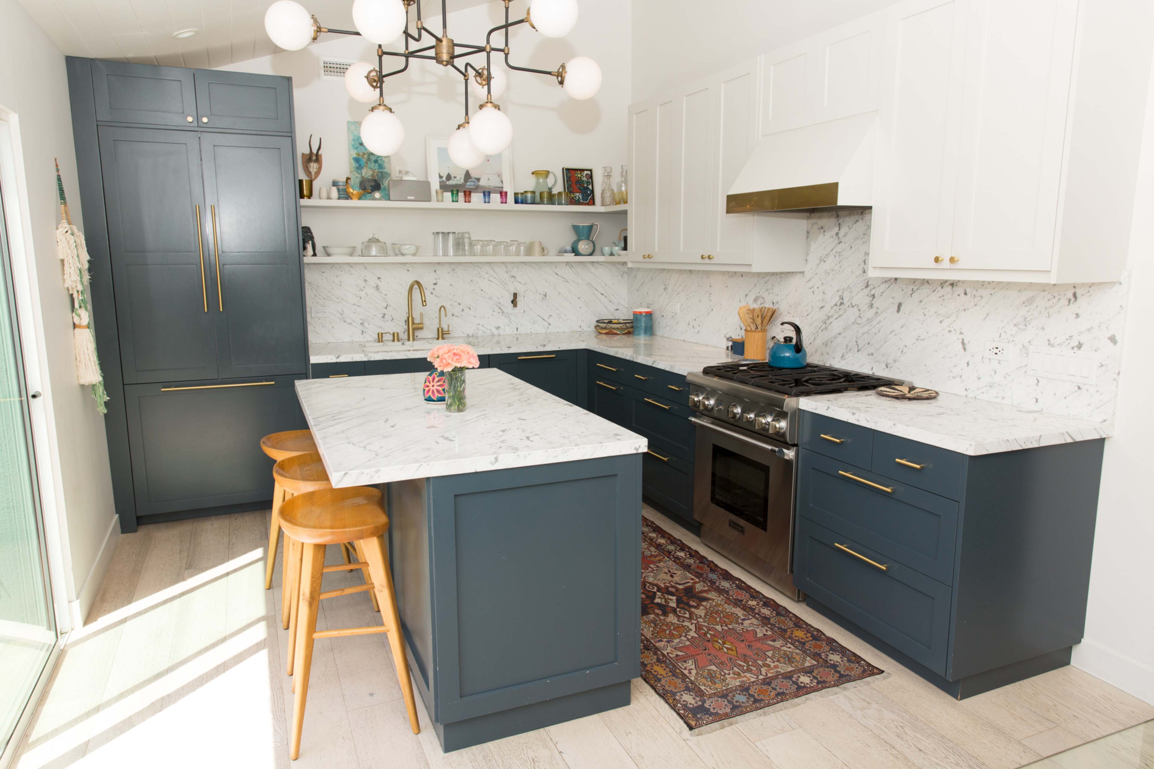 A modern kitchen with navy blue cabinetry, a marble countertop, and an arranged layout featuring a stove, sink, and wooden bar stools.