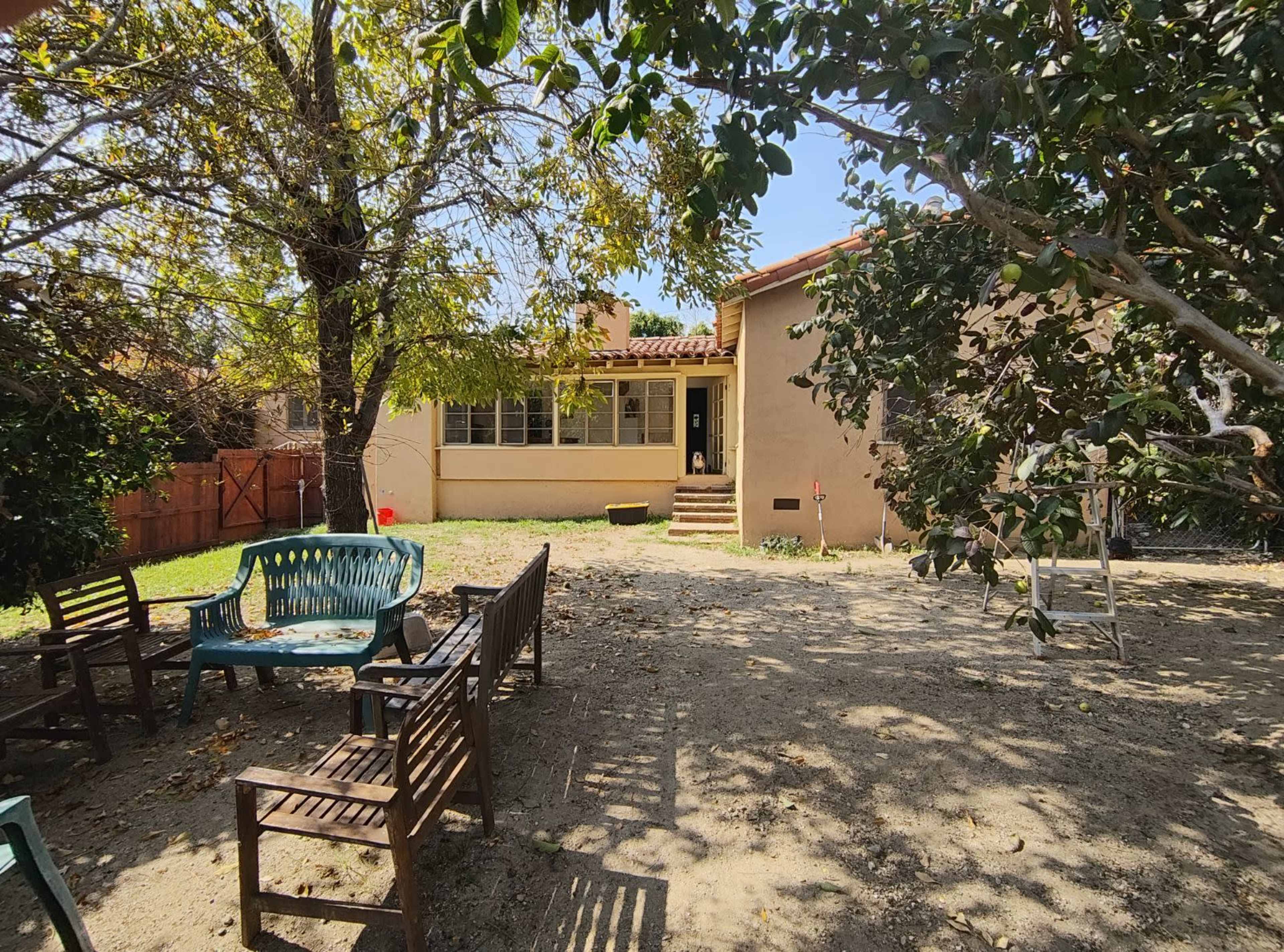 A backyard with a patio area, featuring wooden furniture and a house in the background under a clear blue sky.
