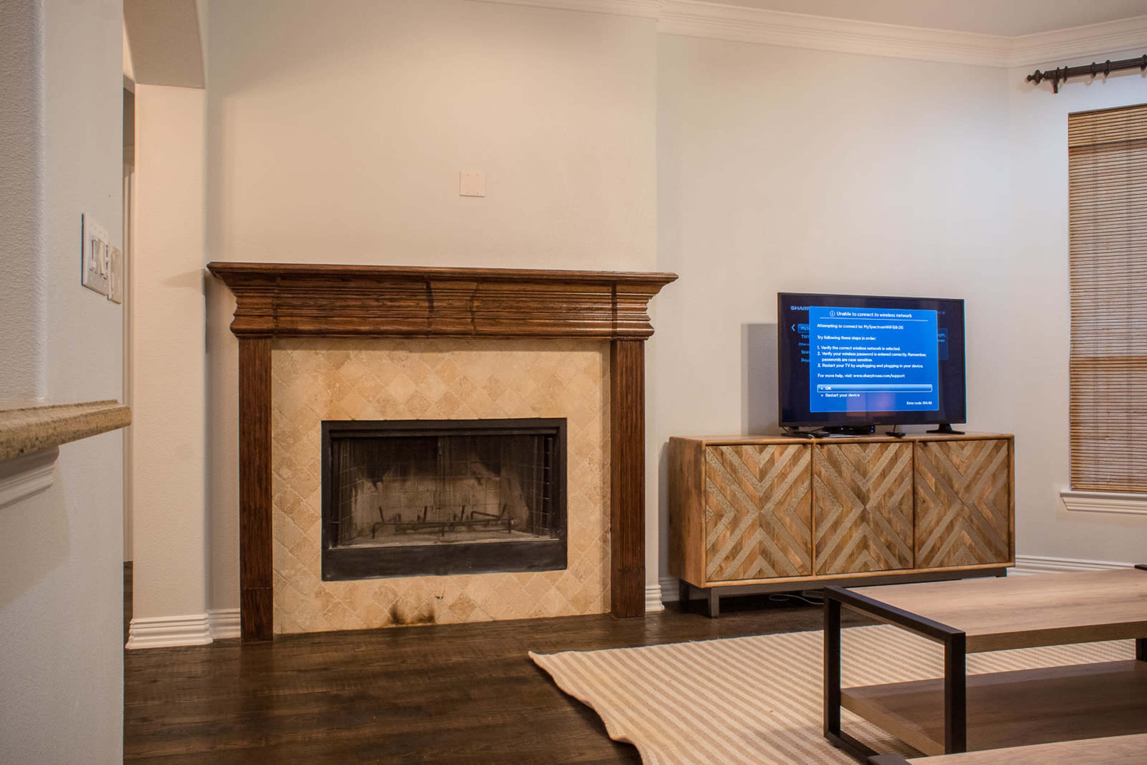 A living room with a wooden fireplace mantel, a television on a cabinet, and wooden flooring.