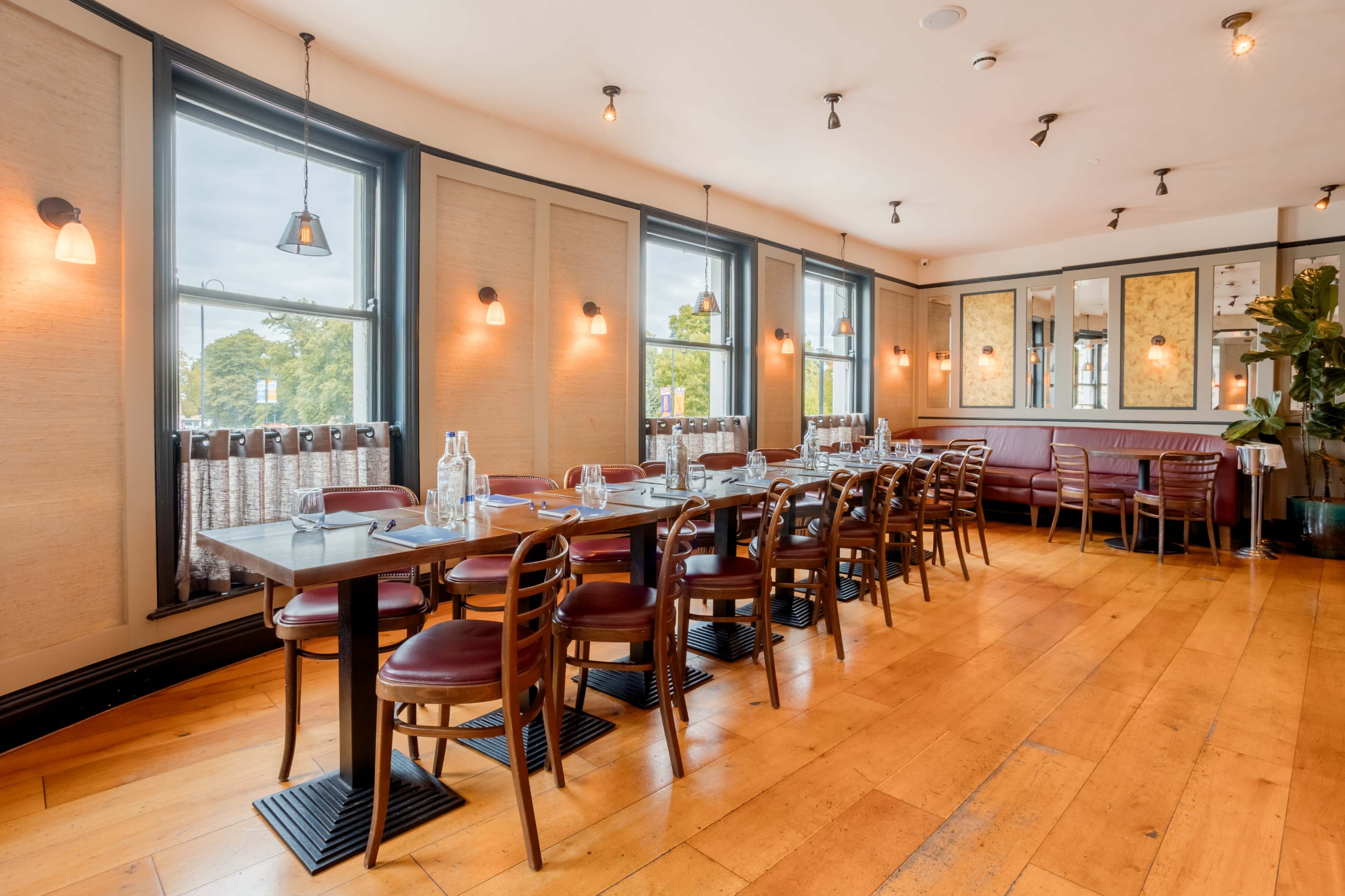 The image shows a spacious dining area with wooden floors, large windows, and tables set for multiple guests.