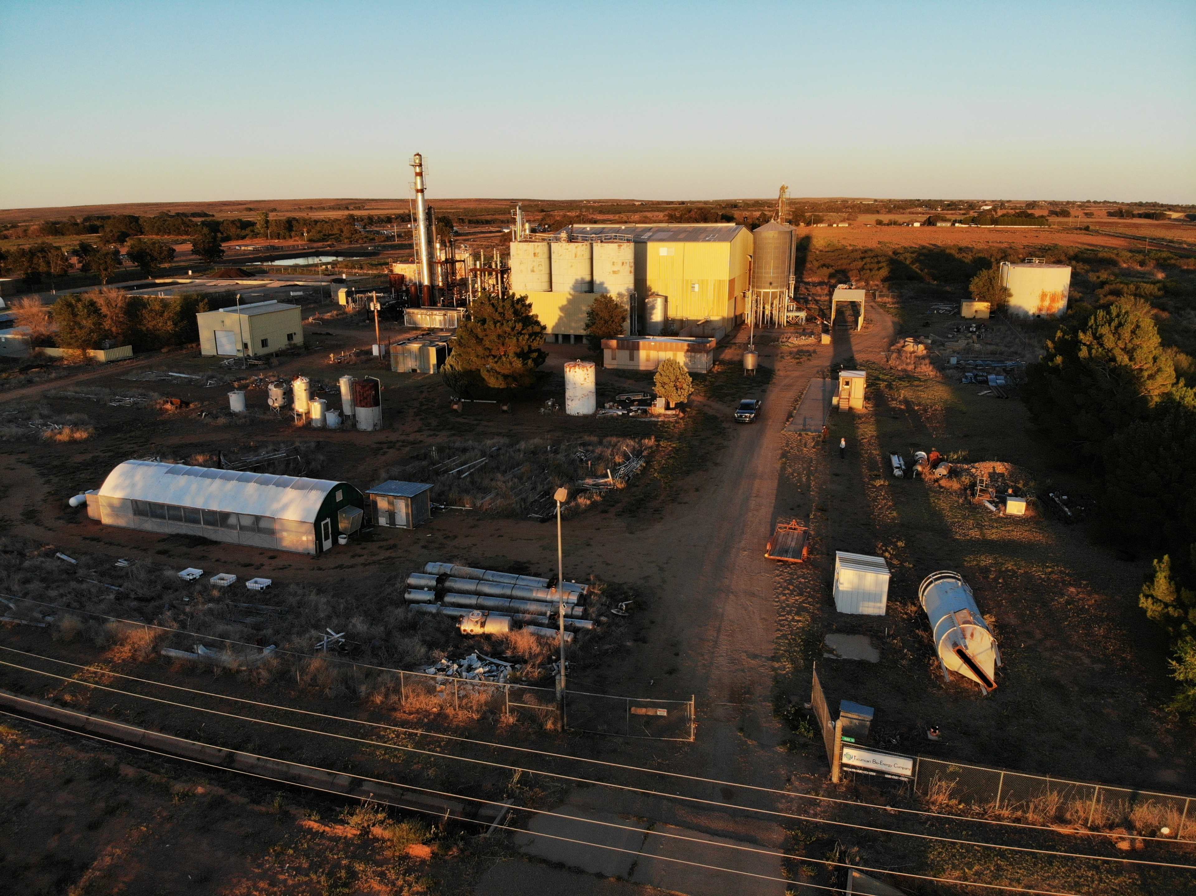 An industrial site featuring storage tanks, buildings, and various equipment scattered across a landscape during sunset.