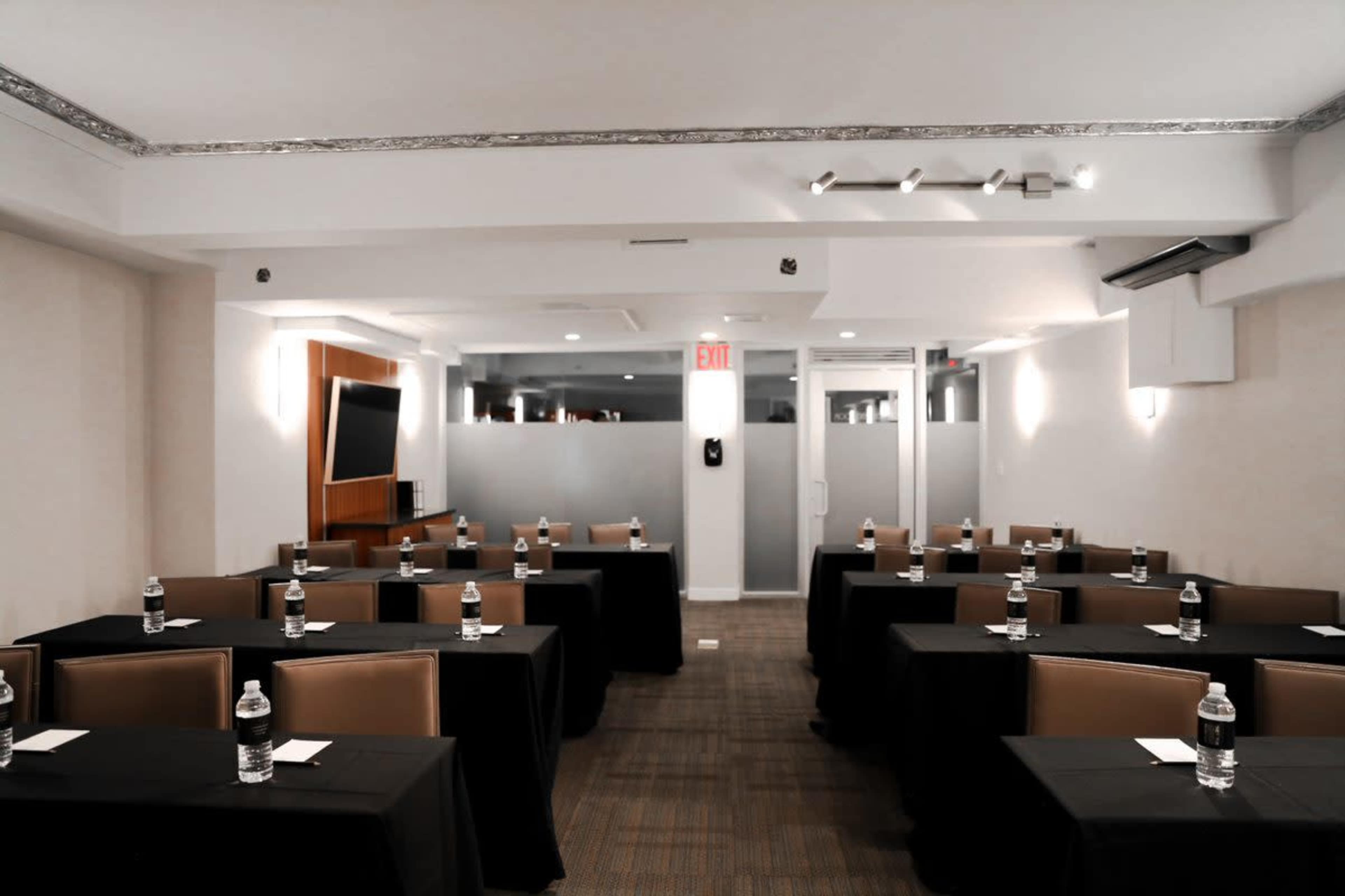 A conference room arranged with several tables covered in black tablecloths, each equipped with a bottle of water and a notepad.