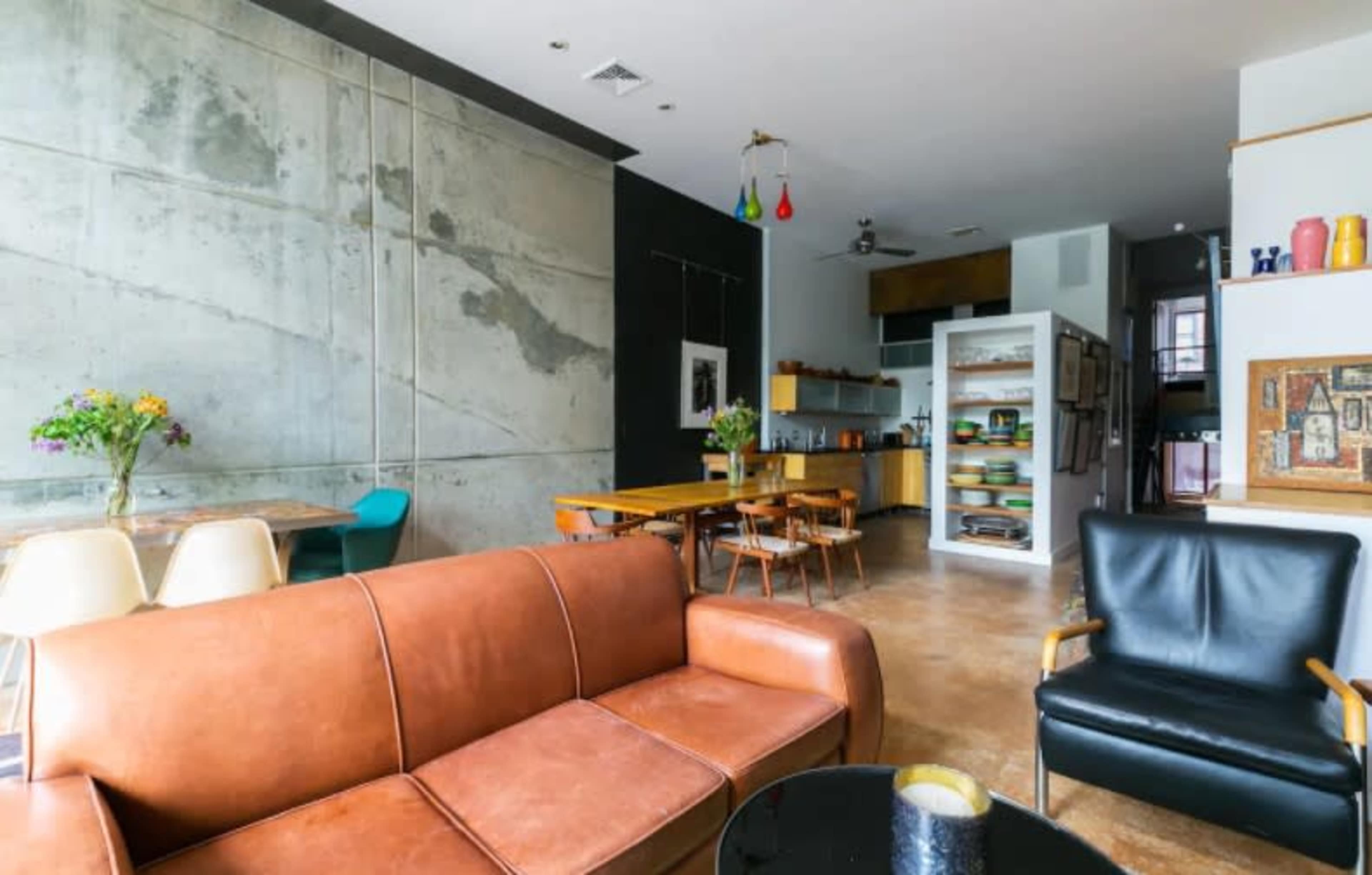 A modern living space with a concrete wall, wooden furniture, and a kitchenette in the background.