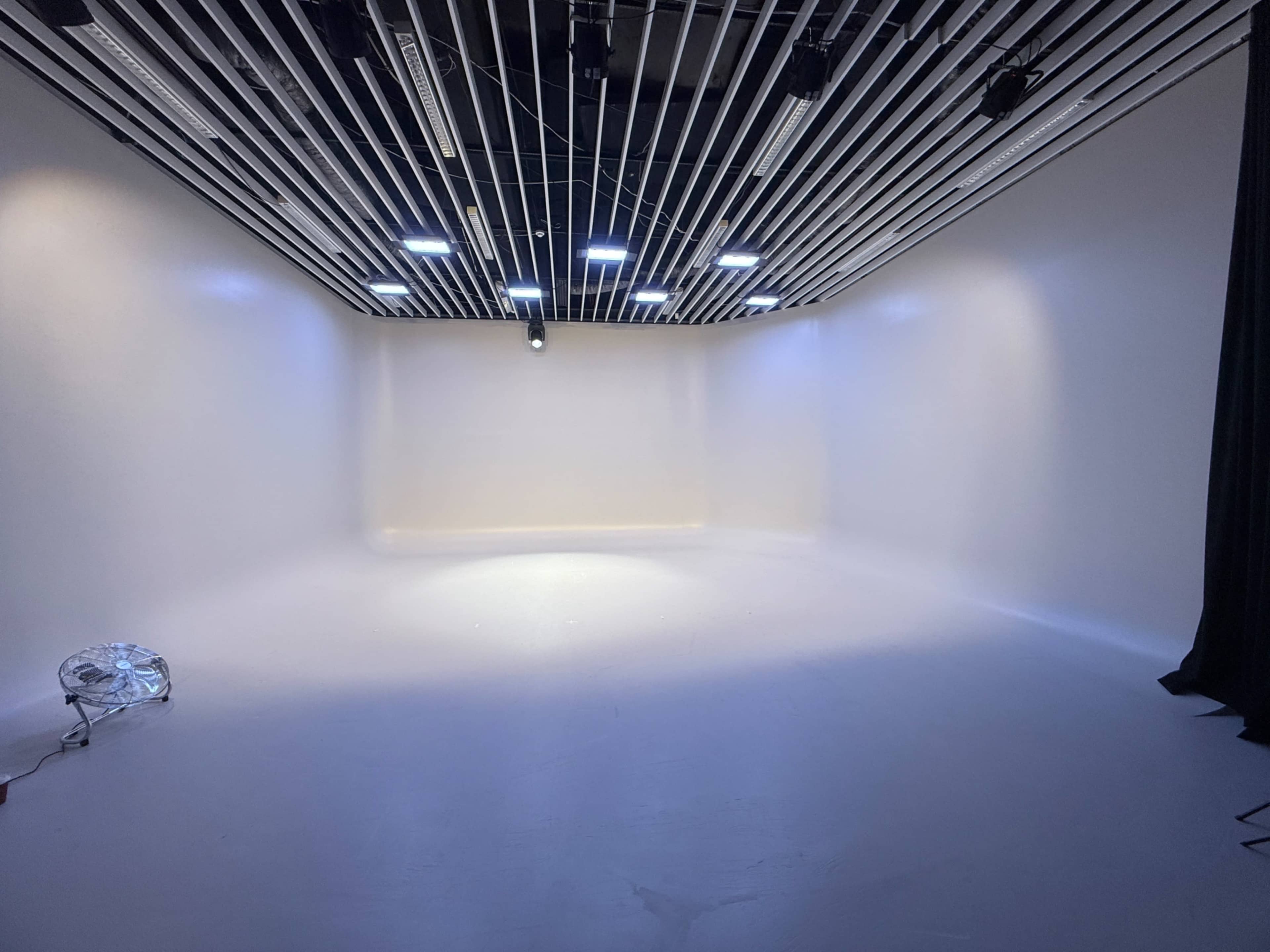 A bright, empty studio space features white walls and a ceiling with rows of overhead lights.