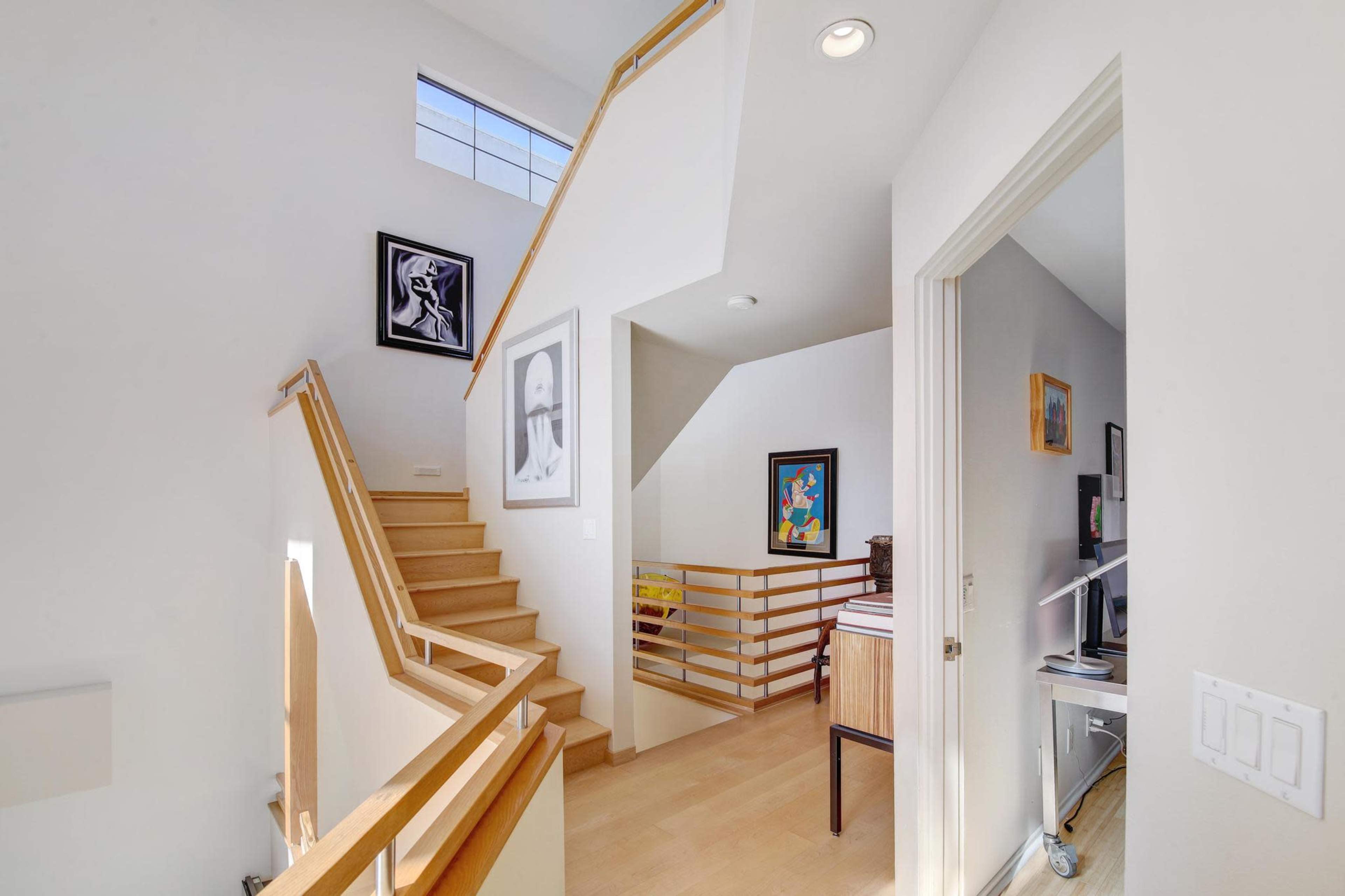 The image shows a bright, modern stairway with wooden steps and framed artwork on the walls.
