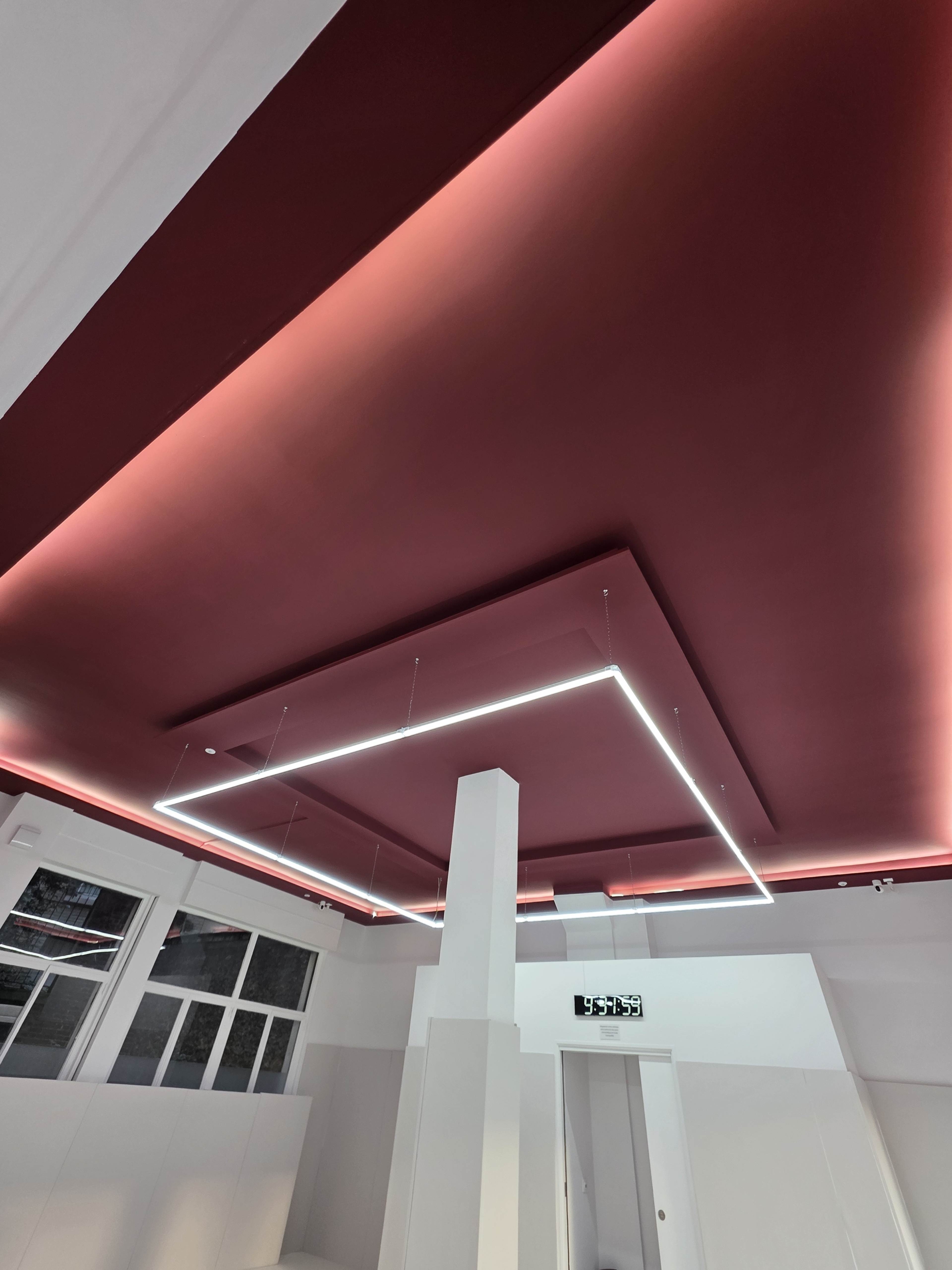 The image shows a modern interior space with a deep red ceiling highlighted by rectangular LED lighting.