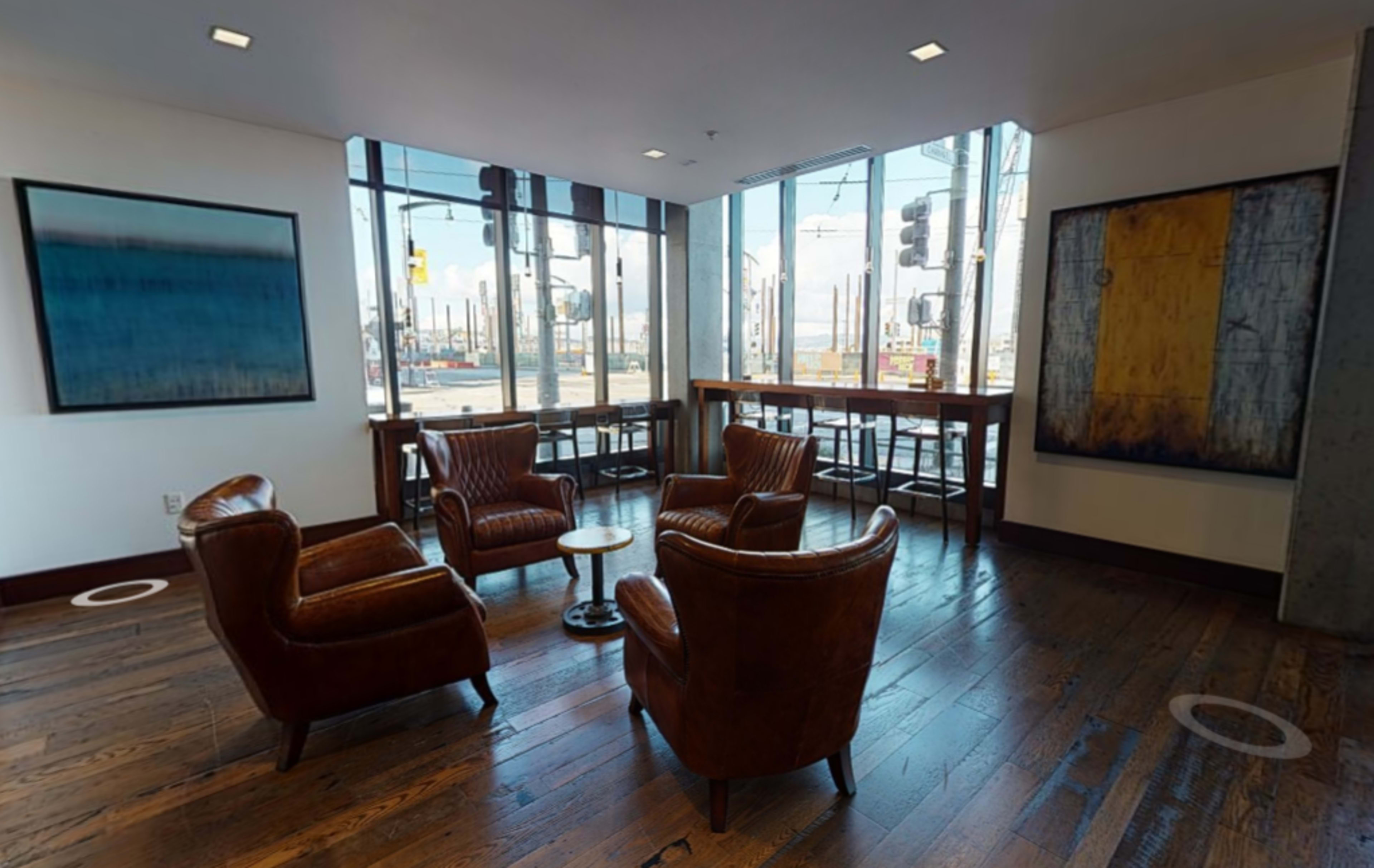 A corner seating area with two brown leather chairs and a small round table, next to large windows overlooking a city street and traffic signals.
