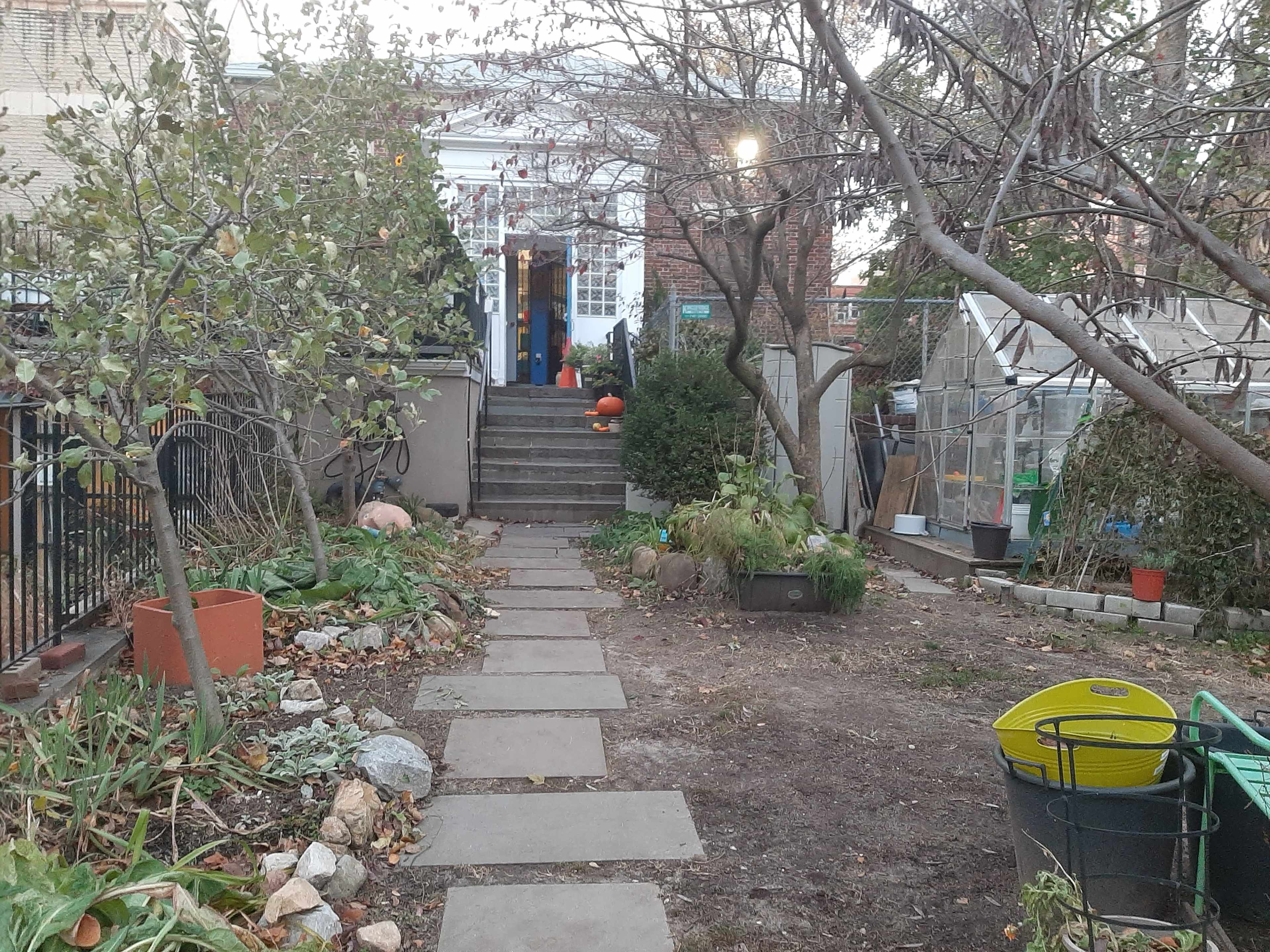 A pathway of stone slabs leads to a set of stairs ascending to a building, flanked by plants and trees on either side.