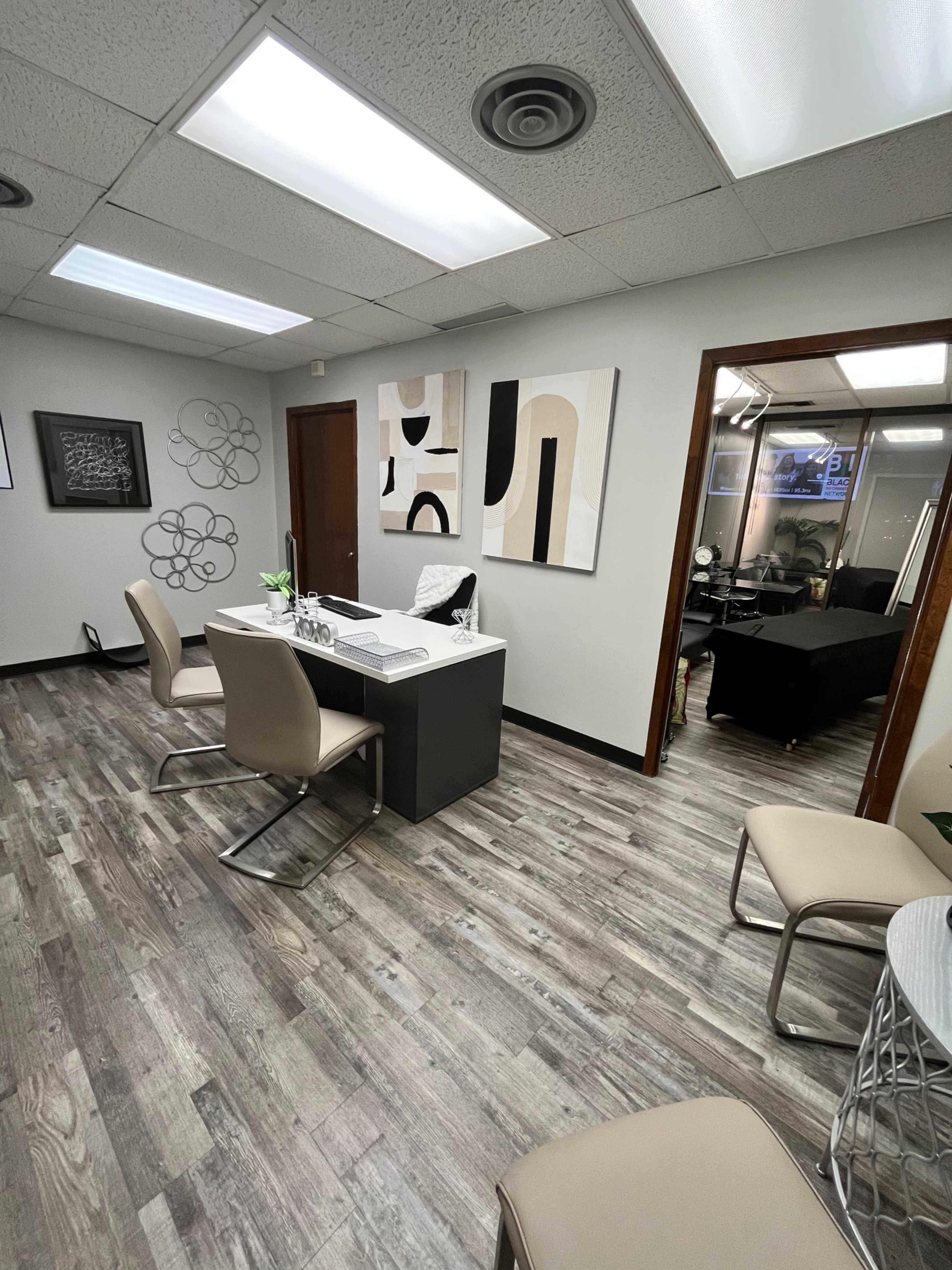 A modern office interior with a reception area featuring a small desk and four chairs, along with abstract artwork on the walls.