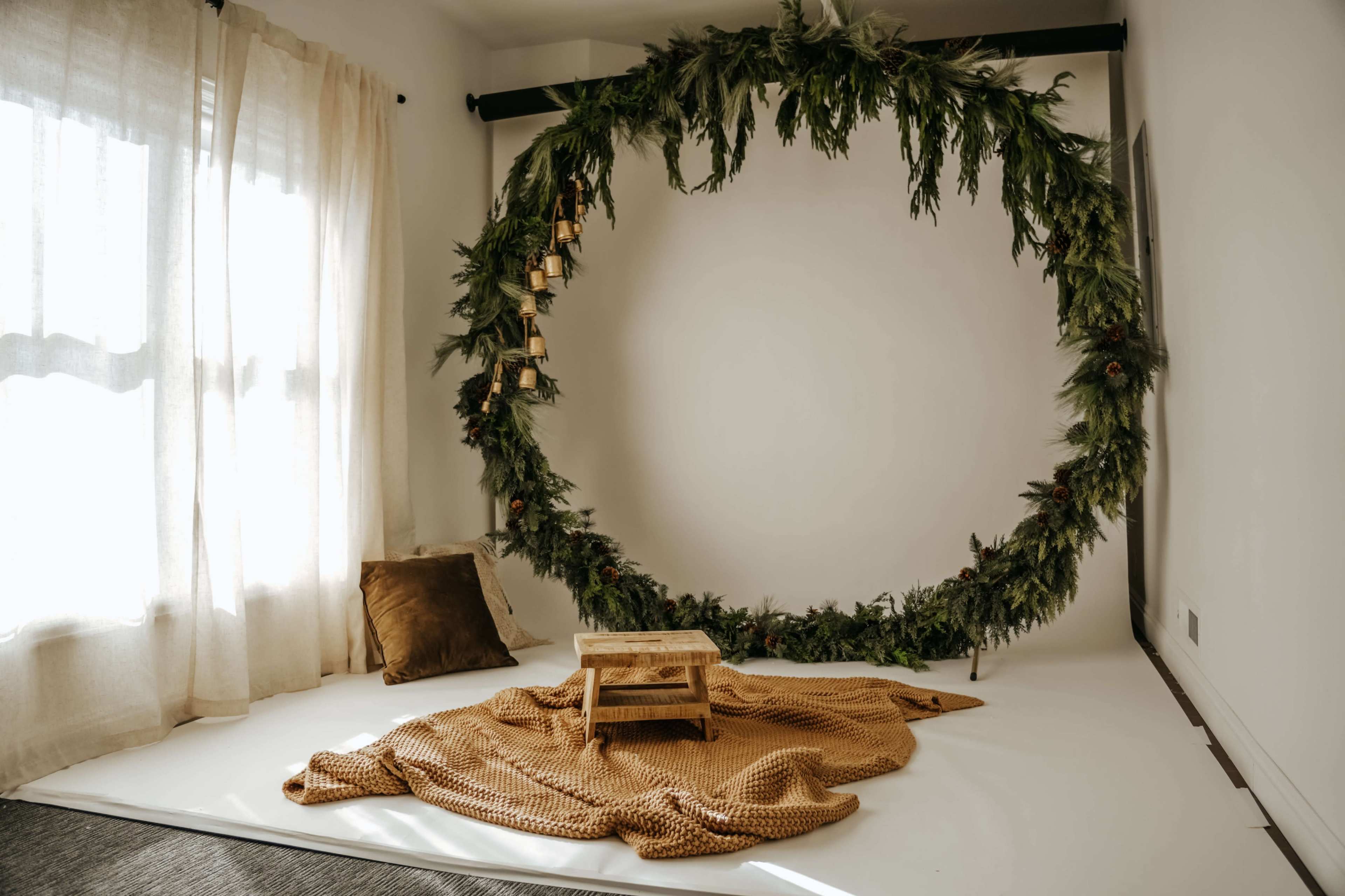 The image shows a simple indoor setting with a circular greenery installation on a plain wall, a small wooden table, and a cozy blanket on the floor.