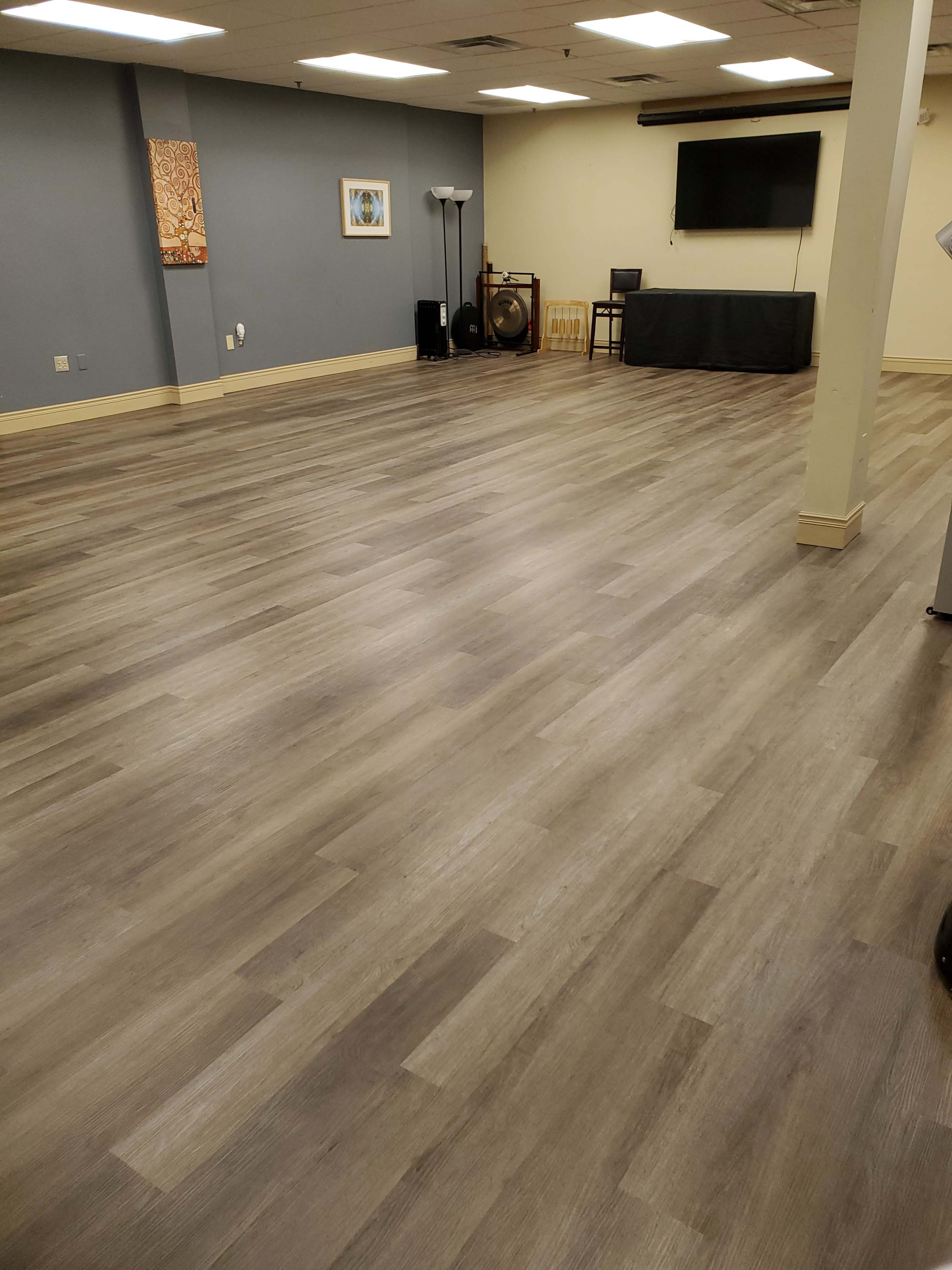 The image shows an empty room with wooden flooring, a gray wall, a TV, and a table at the far end.