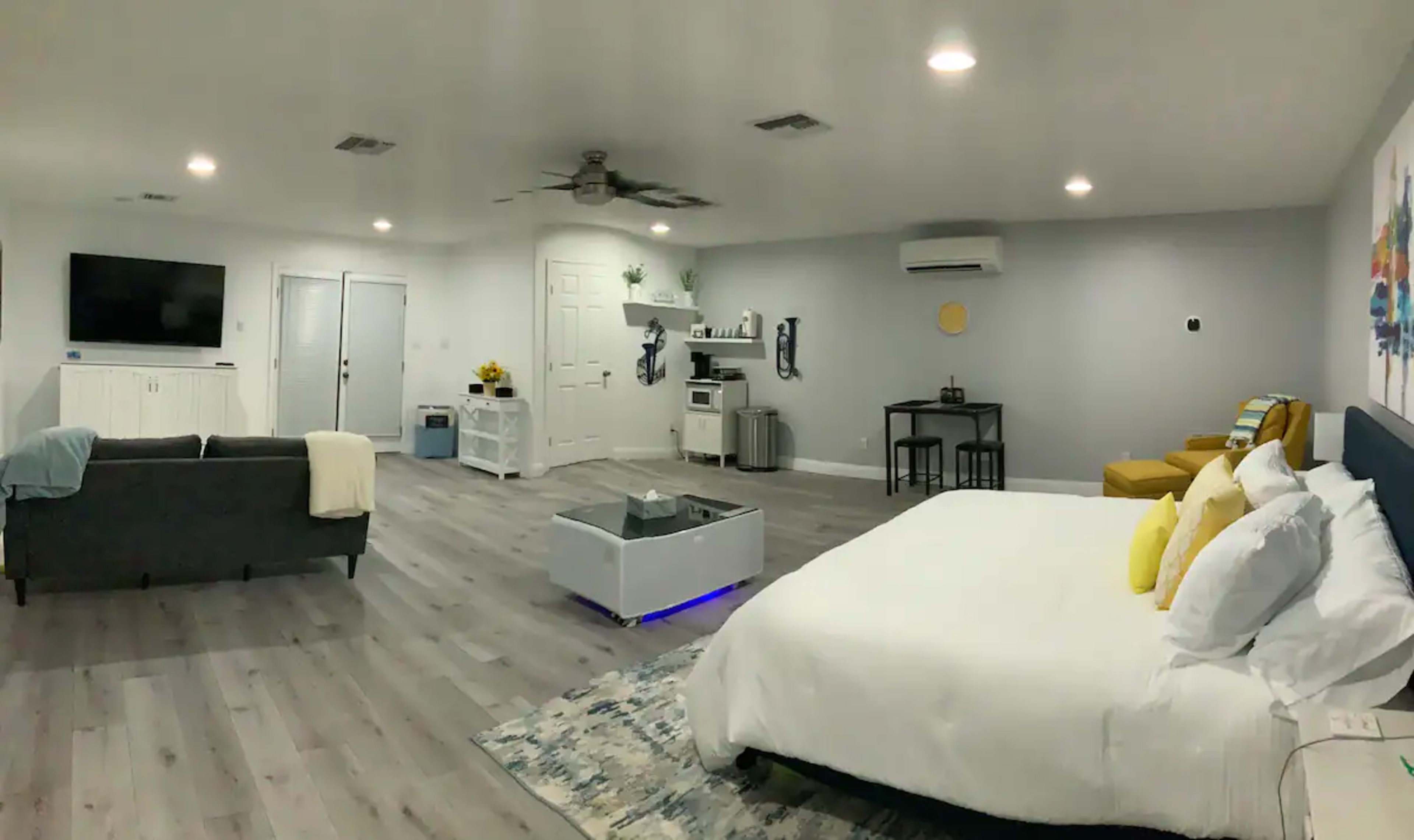 A spacious, modern interior with a bed, seating area, and kitchenette in a well-lit room.