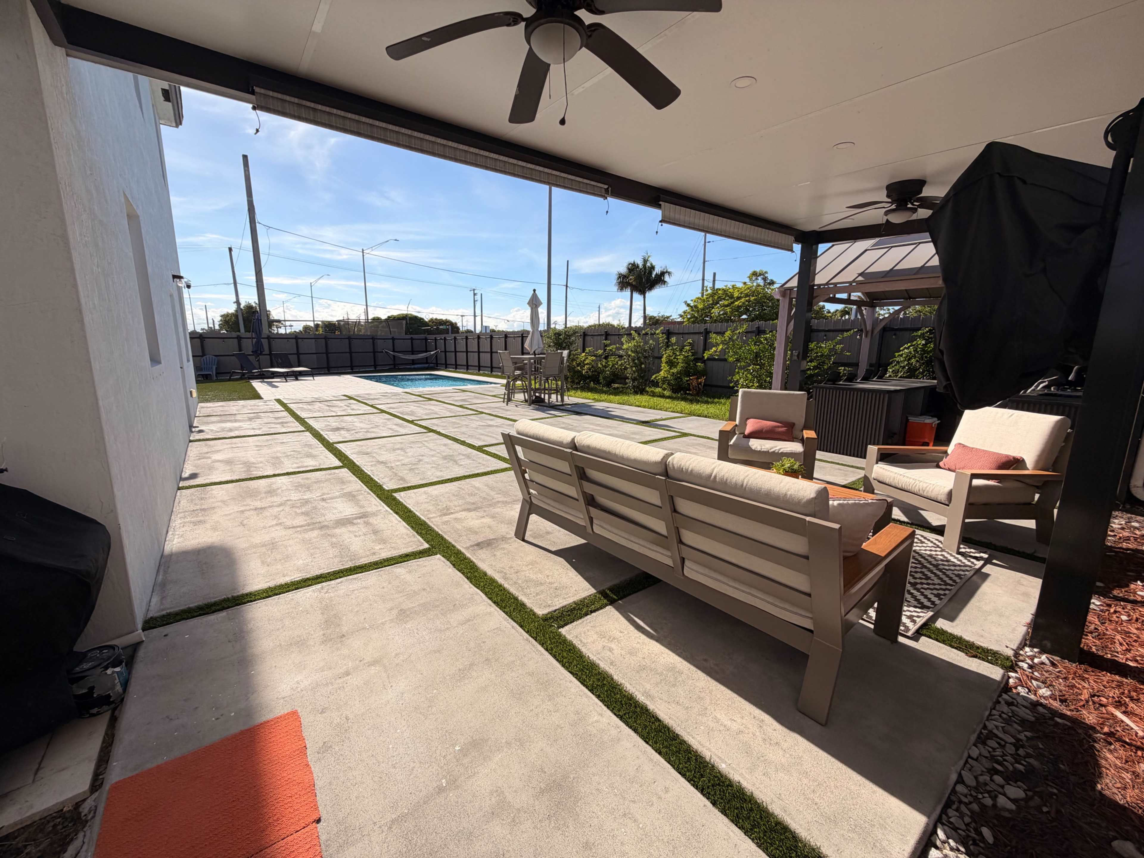 The image shows a backyard patio area with outdoor seating, a swimming pool, and a well-maintained lawn.