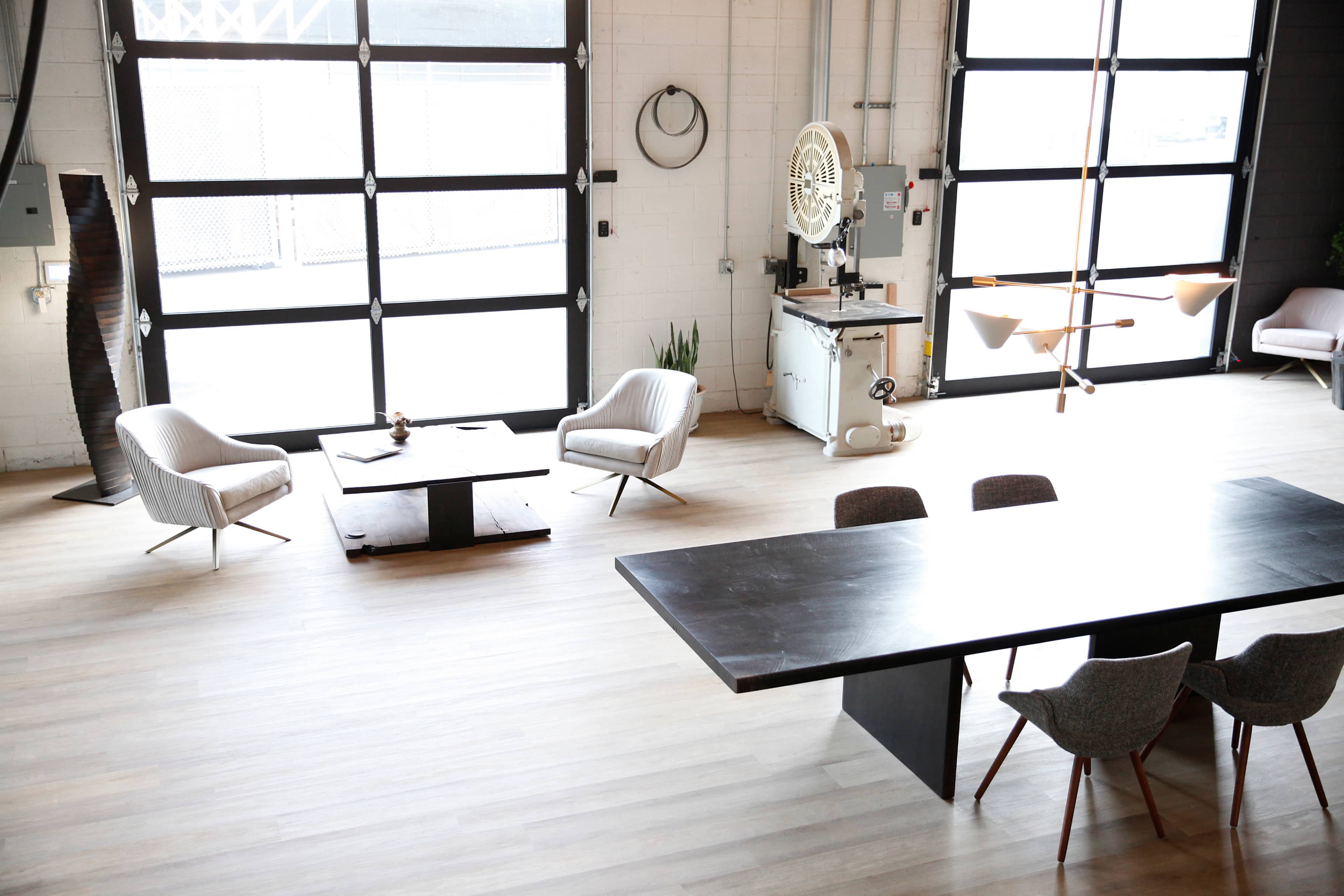 A spacious interior with a large table and chairs, two armchairs, and large windows letting in natural light.