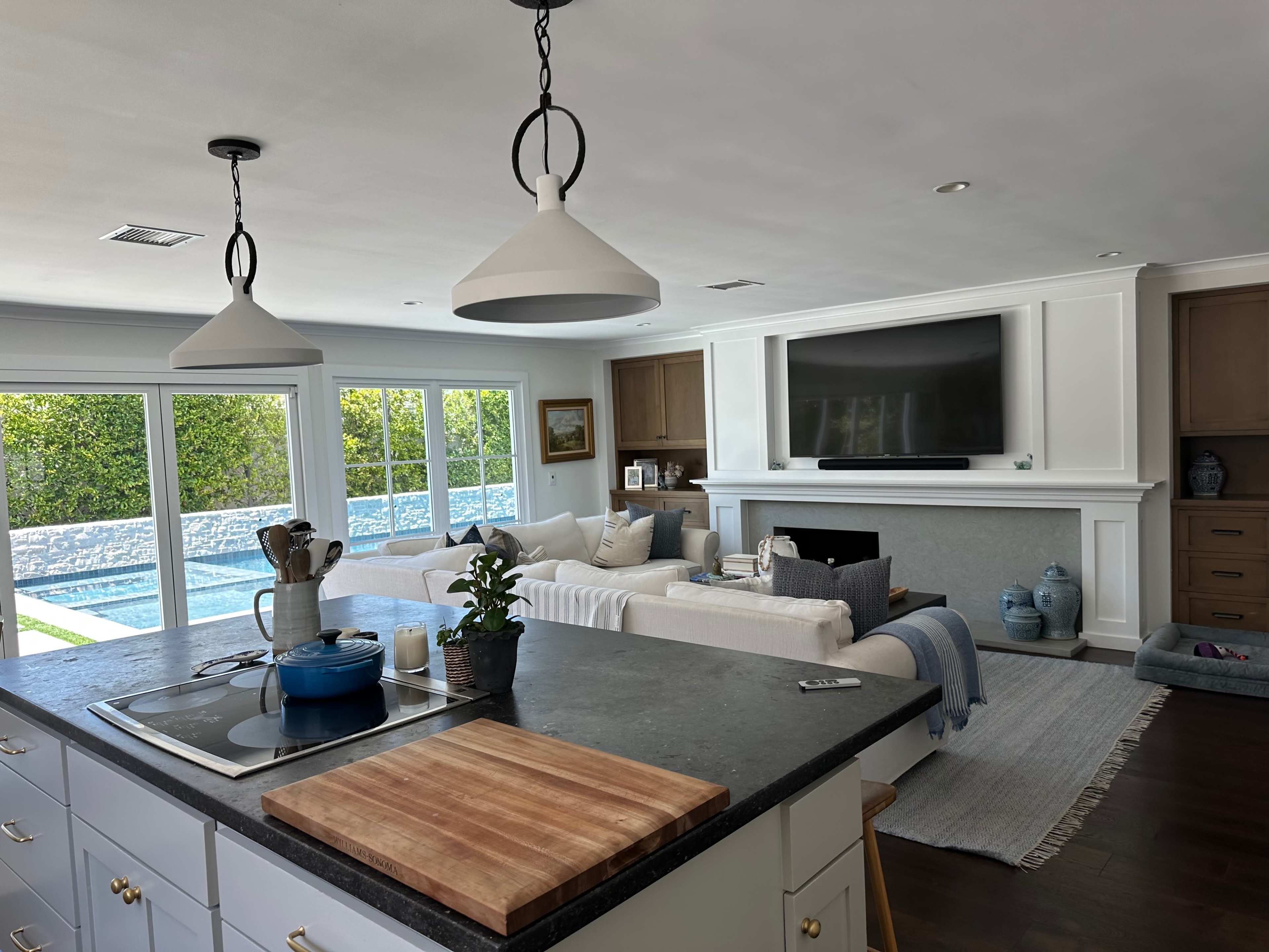 A bright, modern living room features a large television, a sectional sofa, and a view of a pool through sliding glass doors.