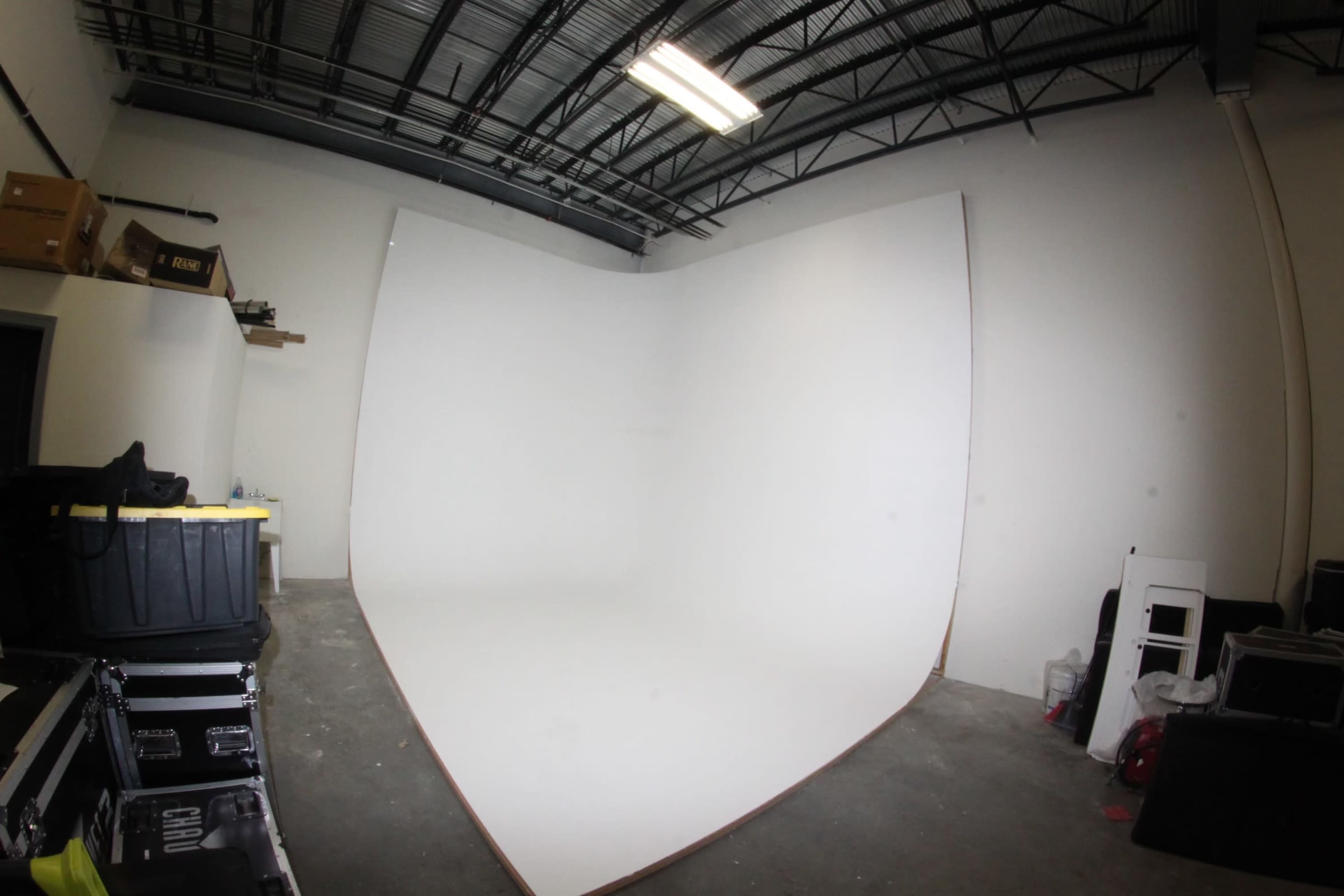 A photography studio with a large white seamless backdrop and various storage containers and equipment along the walls.