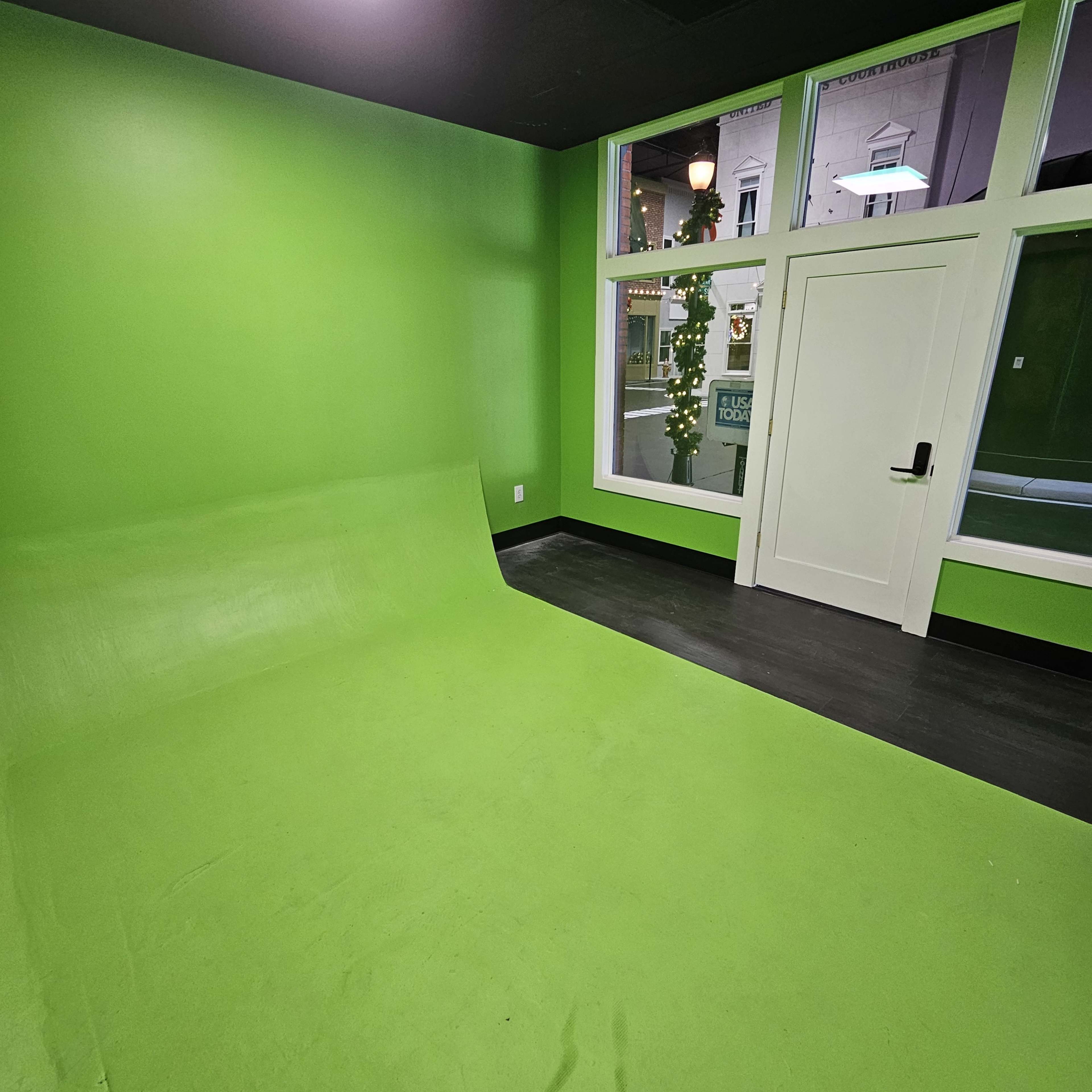 The image shows a room with bright green walls and a green floor covering, featuring a large window and a white door.
