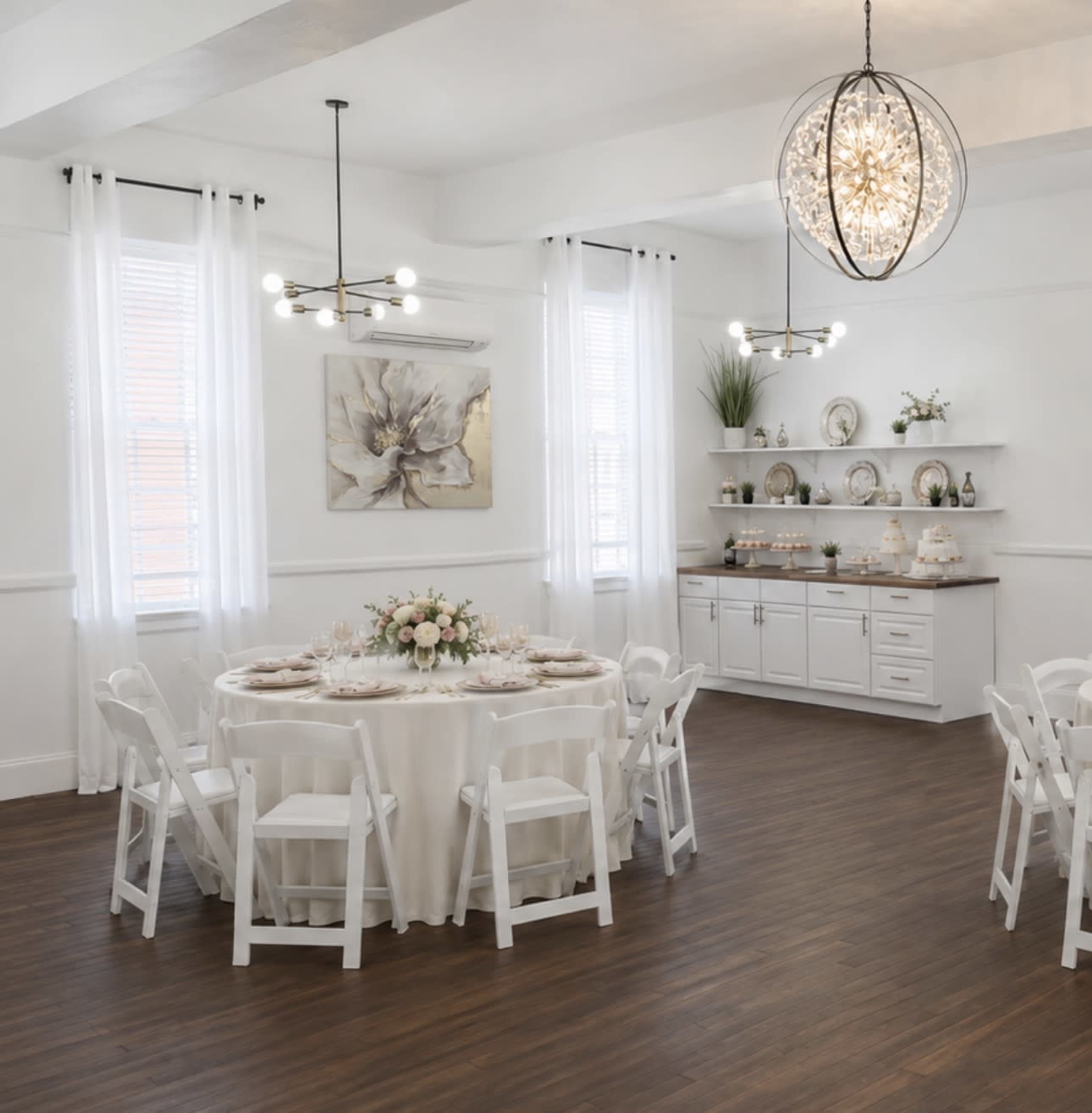 A well-arranged event space features a round table set with elegant tableware, surrounded by white chairs, and a decorative shelf displaying plates and floral decor.