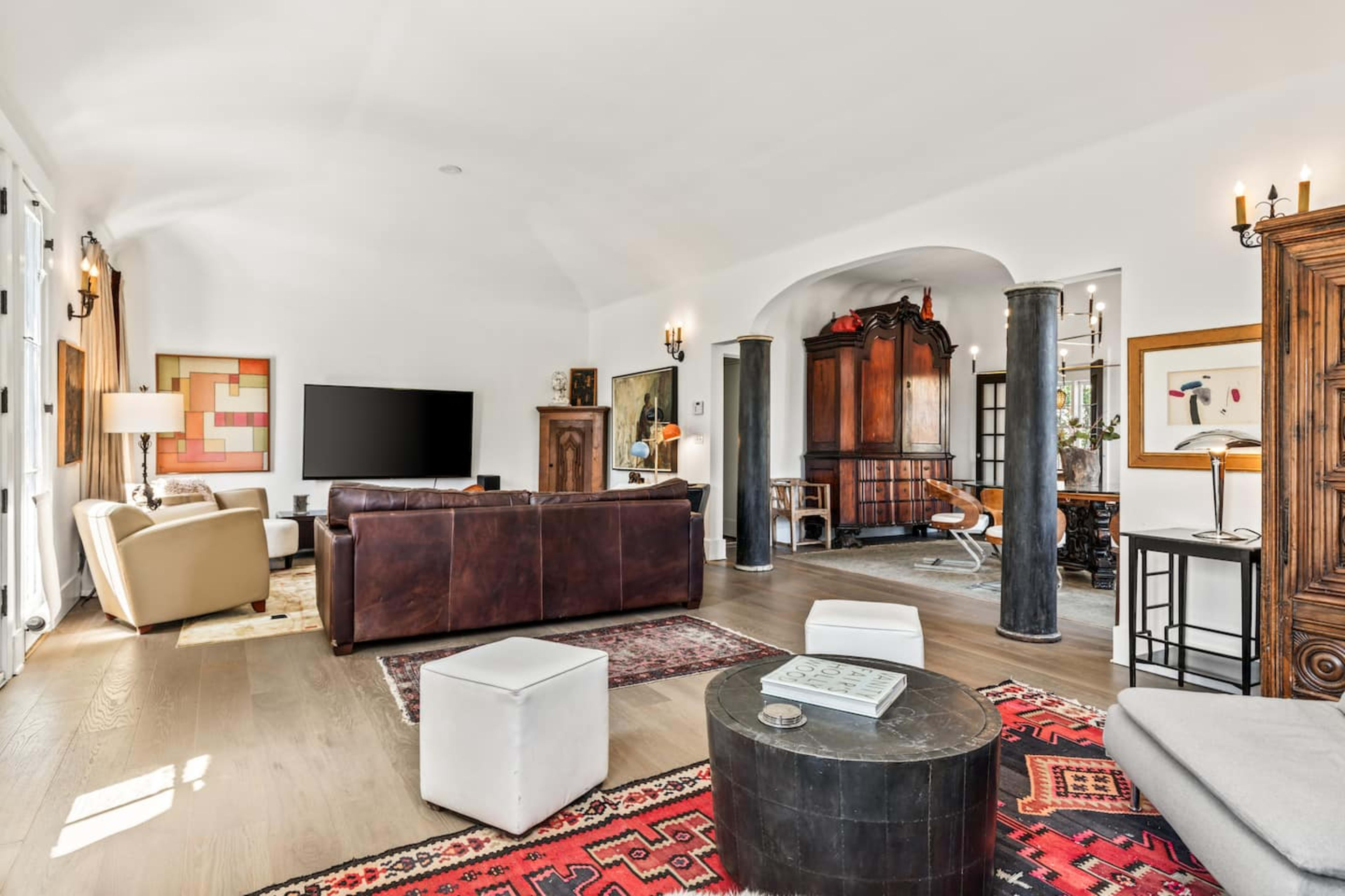 The image shows a spacious living room featuring a large leather sofa, a modern flat-screen TV on the wall, and a mix of contemporary and traditional furniture.