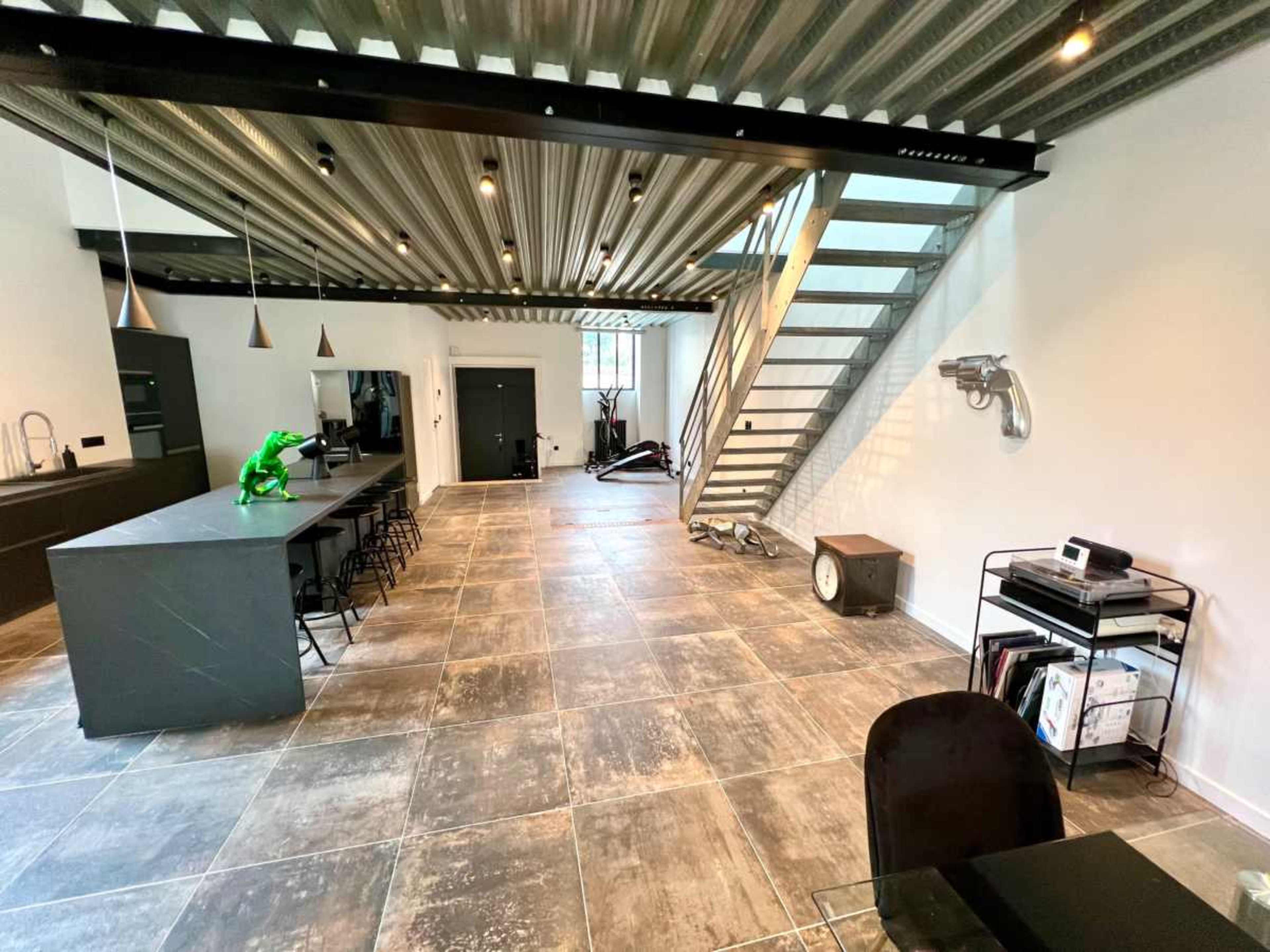 A spacious interior with a modern kitchen island, a green sculpture, and a staircase leading to an upper level.