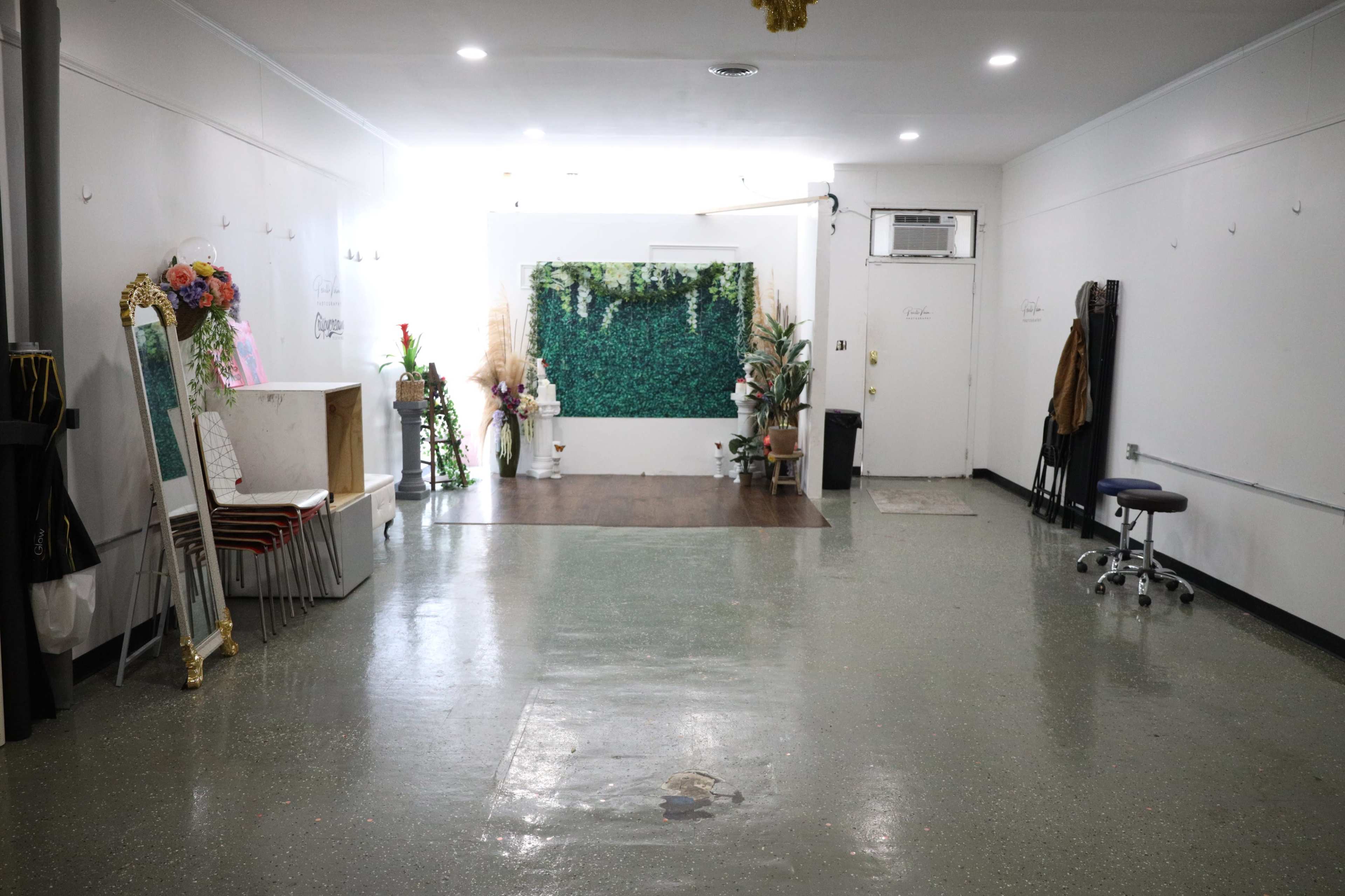 An empty room features a decorated wall of greenery, a small table, and several plants arranged around a polished floor.