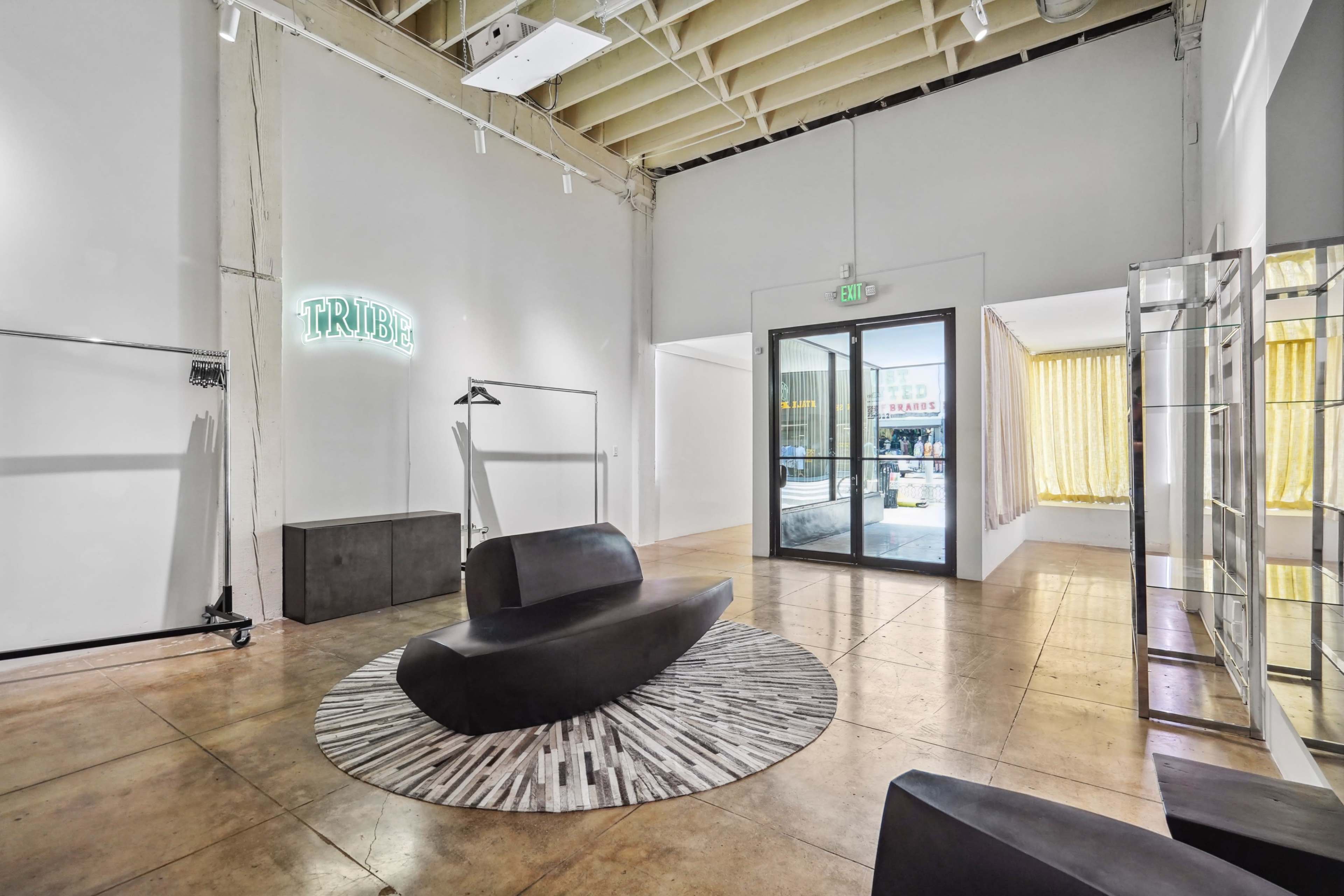 A modern interior space featuring a black curved sofa, a circular patterned area rug, and large windows with sheer curtains.