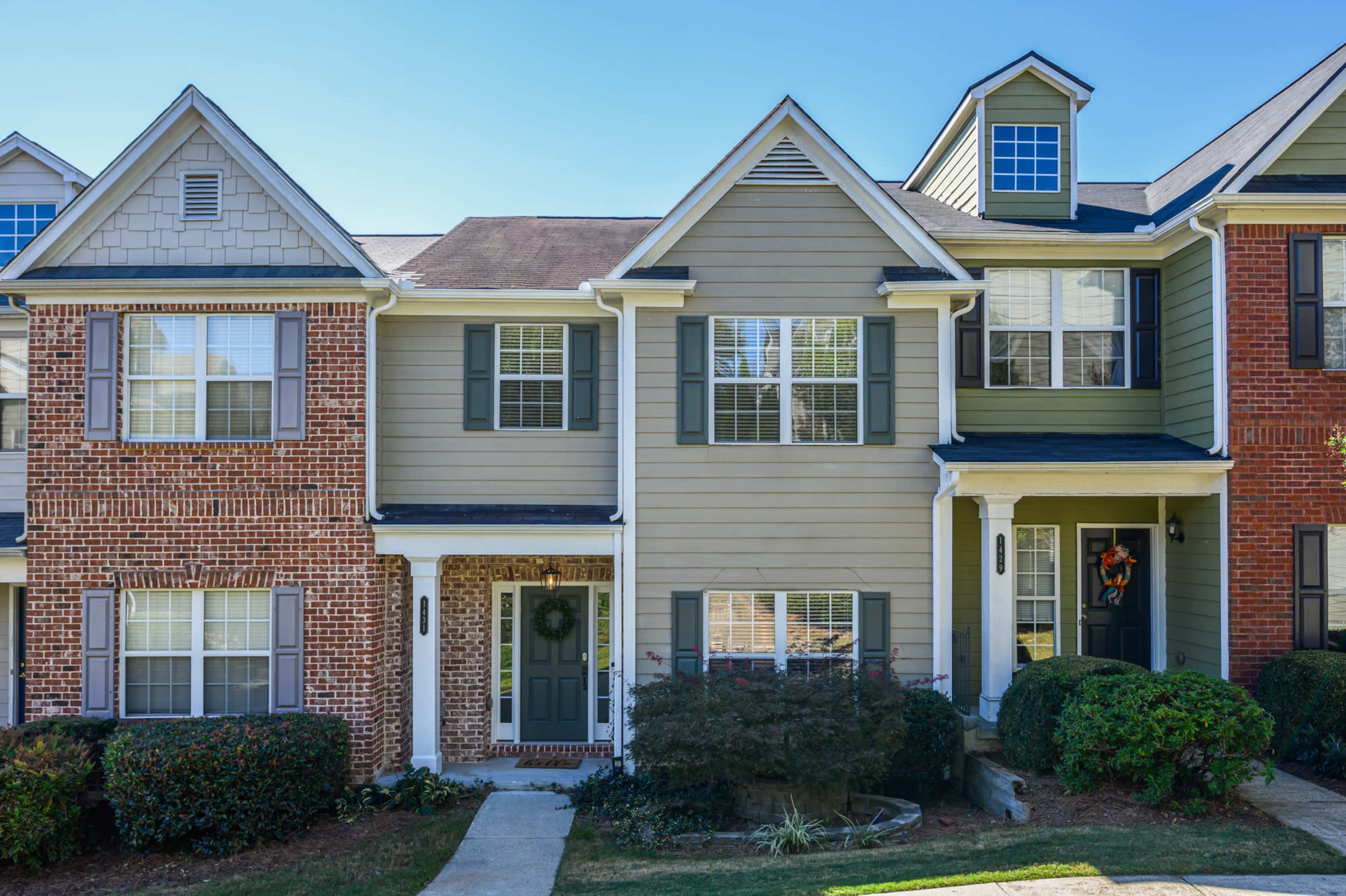 A row of suburban townhouses, featuring a mix of brick and wood siding, with neatly trimmed shrubs and well-defined doorways.