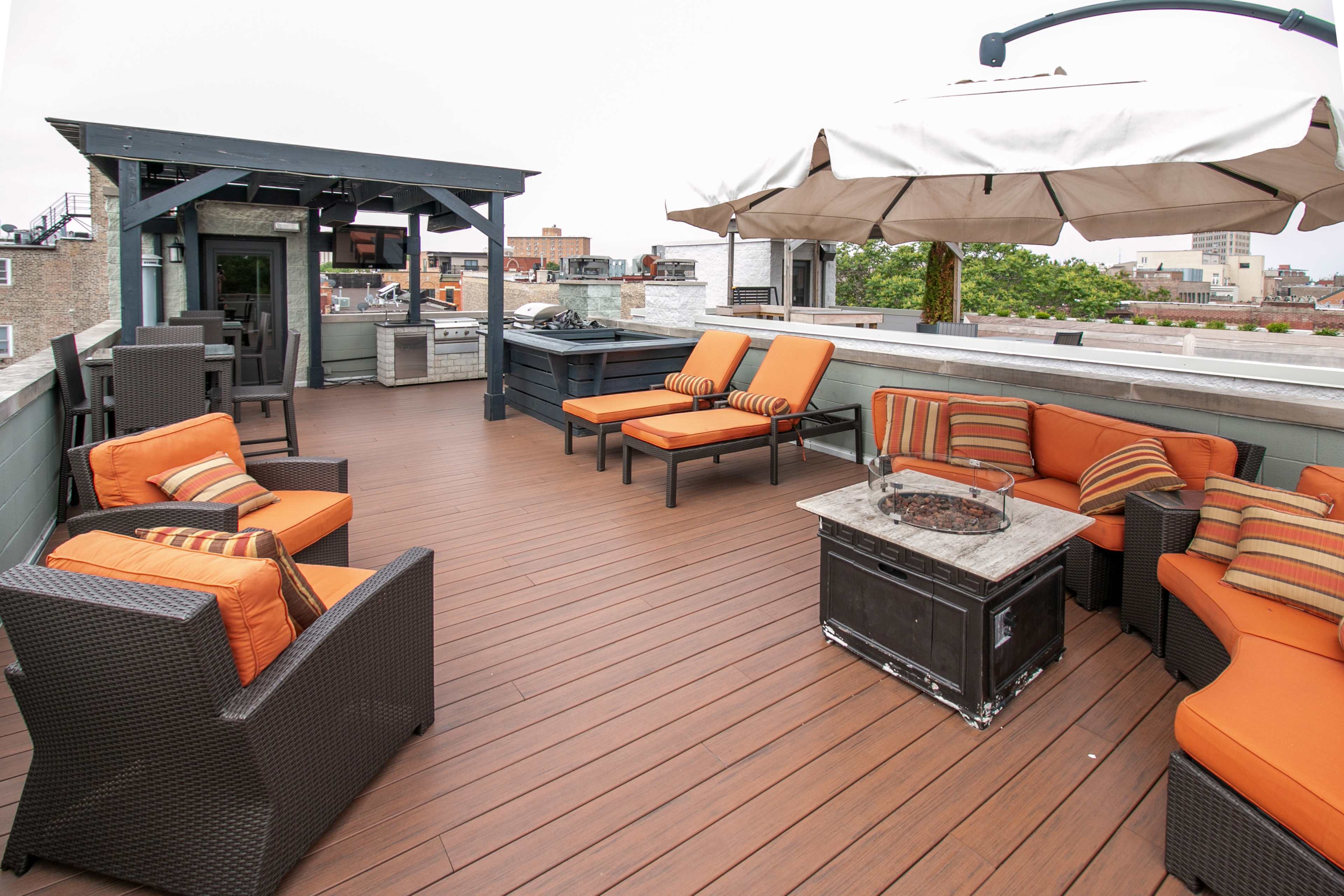 The rooftop terrace features a seating area with orange cushions, a fire pit table, and an outdoor kitchen sheltered by a pergola.